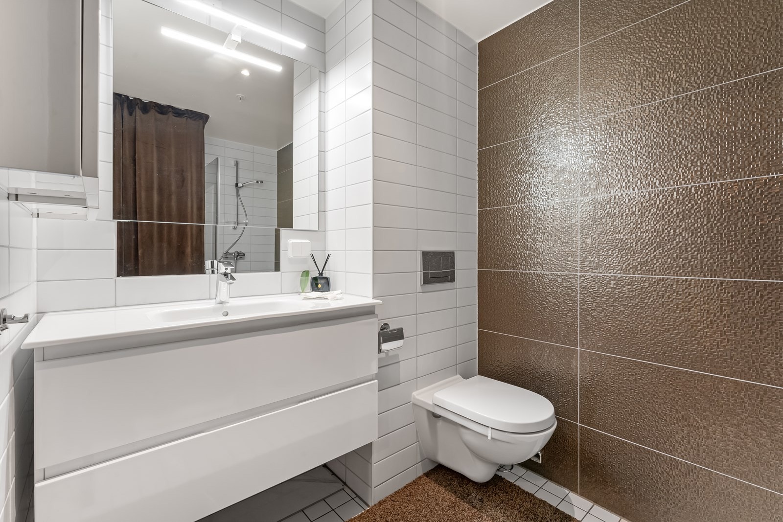 Bad to med bred skuffeinnredning med helstøpt porselens servant og veggskap med høyglanspolerte fronter. Galleribilde