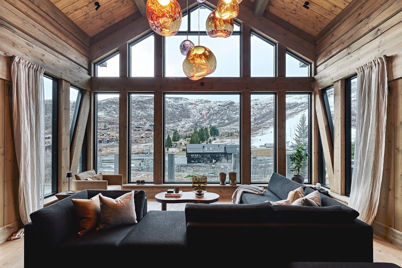 Ved sofagruppa i stuen er det takhøyde opp til 3.etg og panoramautsikt over skibakken. Stuen er innredet med eksklusive lamper fra Tom Dixon, polstra møbler fra Slettvoll, bord fra By Bjørkheim og en 120 cm bred peis levert av Brunner. Galleribilde