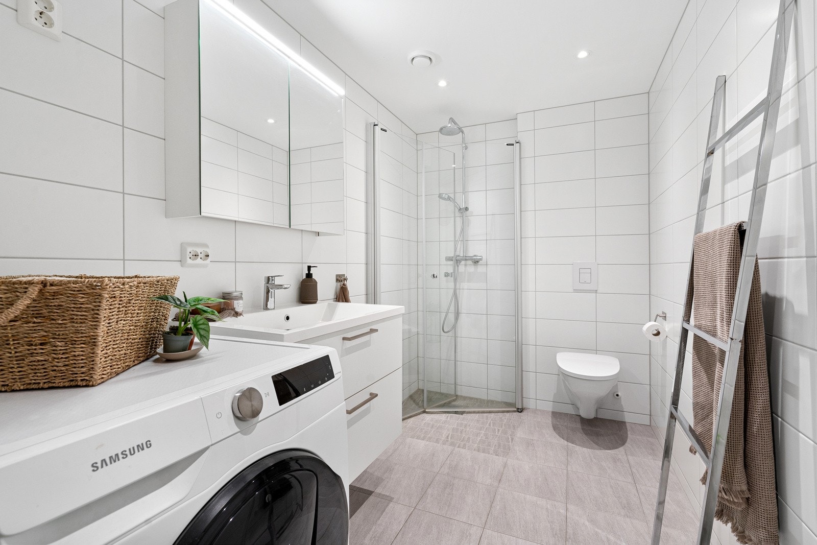 Flislagt bad med gulvvarme. Dusjhjørne med glassvegger og vegghengt dusjarmatur. Servantinnredning og servant med ett-greps armatur. Vegghengt toalett. Galleribilde