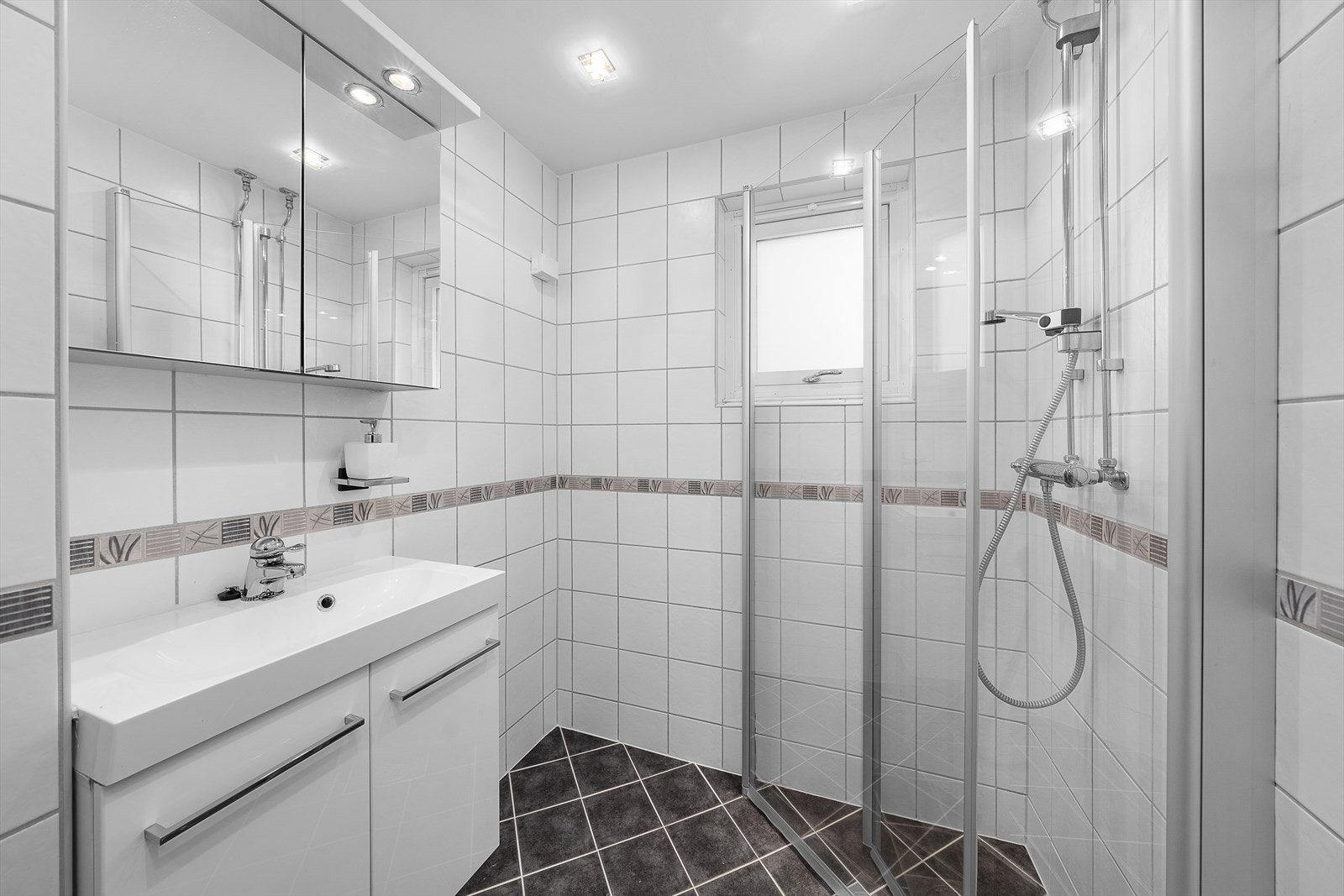Det er gulvvarme og downlights, og badet har vegghengt toalett og et dusjhjørne med innfellbare vegger. Baderomsinnredningen består av servant med hvite underskap og et speilskap med belysning. Galleribilde
