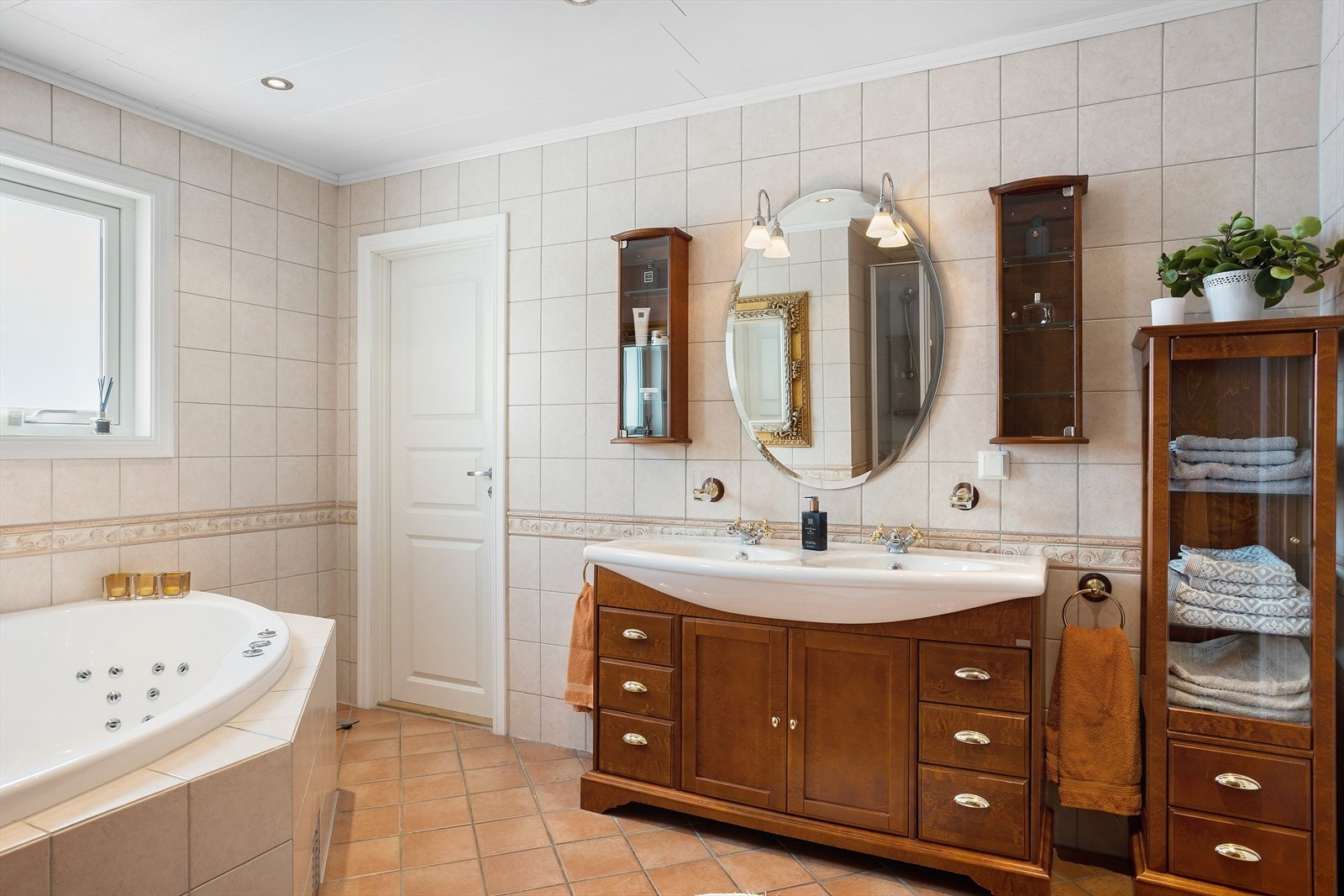 Badet er det heldekkende dusjkabinett, inn fliset boblebadekar, vegg-hengt toalett og heldekkende servantplate med 2 stk. vaskeplasser over innredning med profilerte fronter i en type "edeltre materiale" Galleribilde