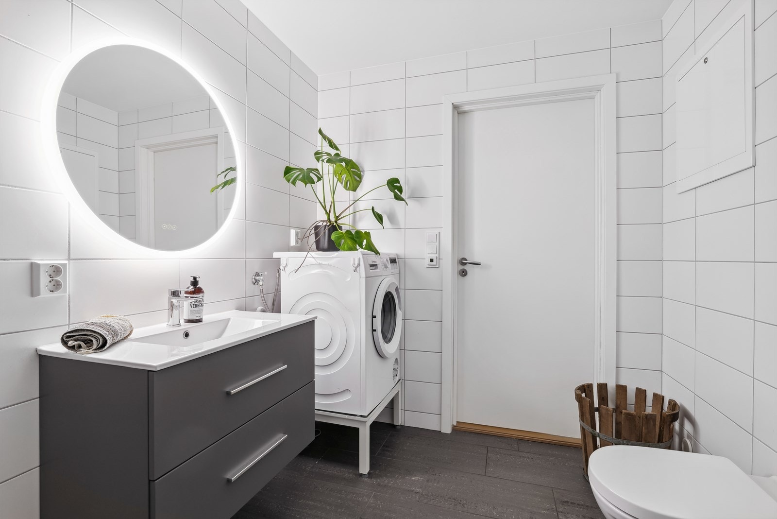 Badet er innredet med et veggmontert toalett, stilren baderomsinnredning, speil med belysning og dusjhjørne med innfellbare dusjdører. Galleribilde