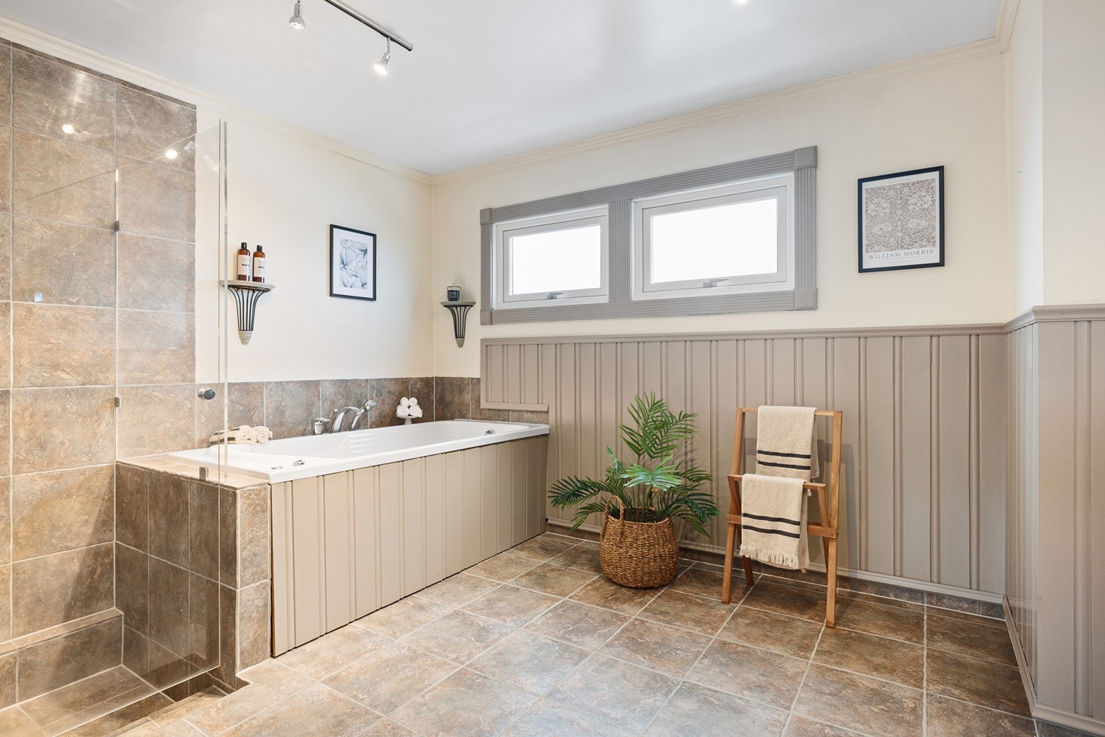 Badet i første etasje har store beige fliser på gulvet med gulvvarme, og fliser på vegger samt malt panel og malte vegger. Galleribilde