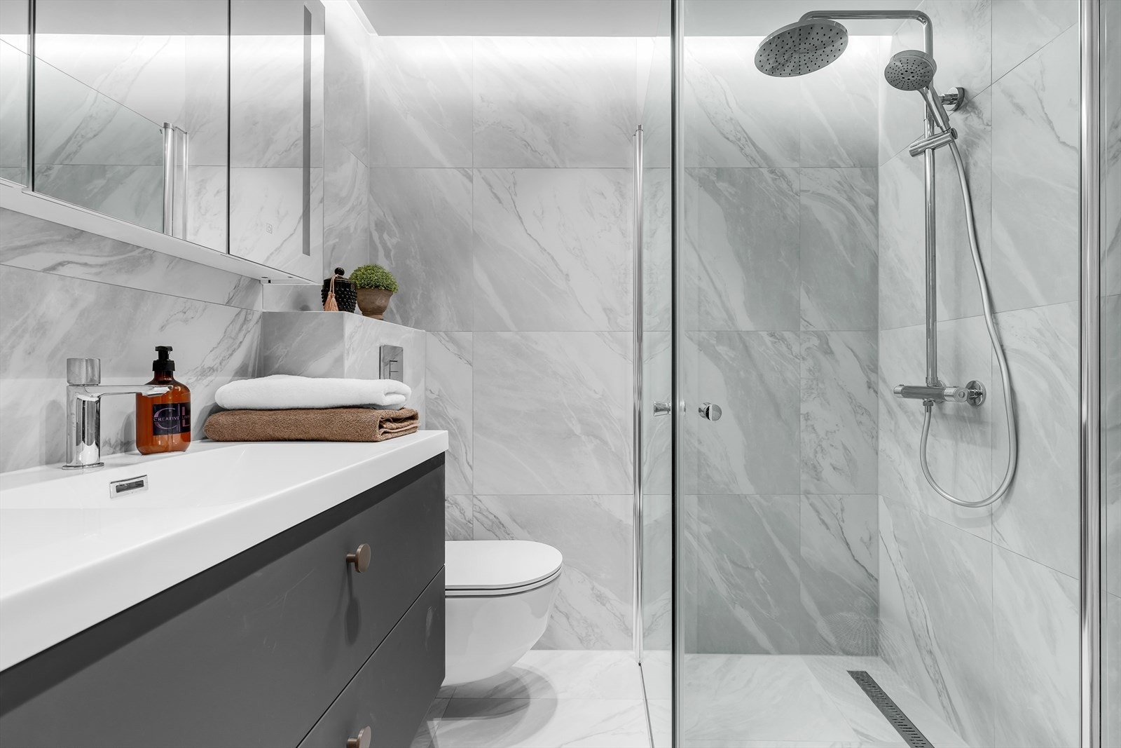 Downlights og indirekte belysning i tak, dusjhjørne med glassvegger, regndusj og hånddusj samt opplegg for vaskemaskin og tørketrommel. Galleribilde