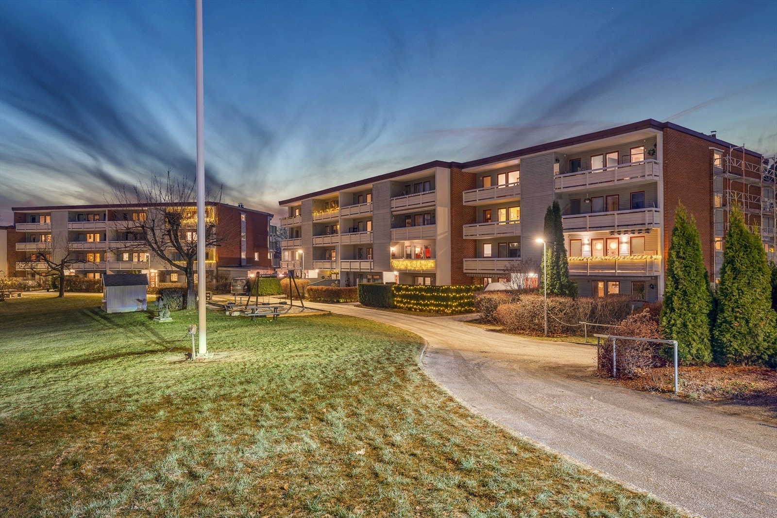 Barnevennlig og bilfri bakgård med asfalterte adkomststier, plen, trær, beplantning, lekeapparater og sittegrupper. Galleribilde