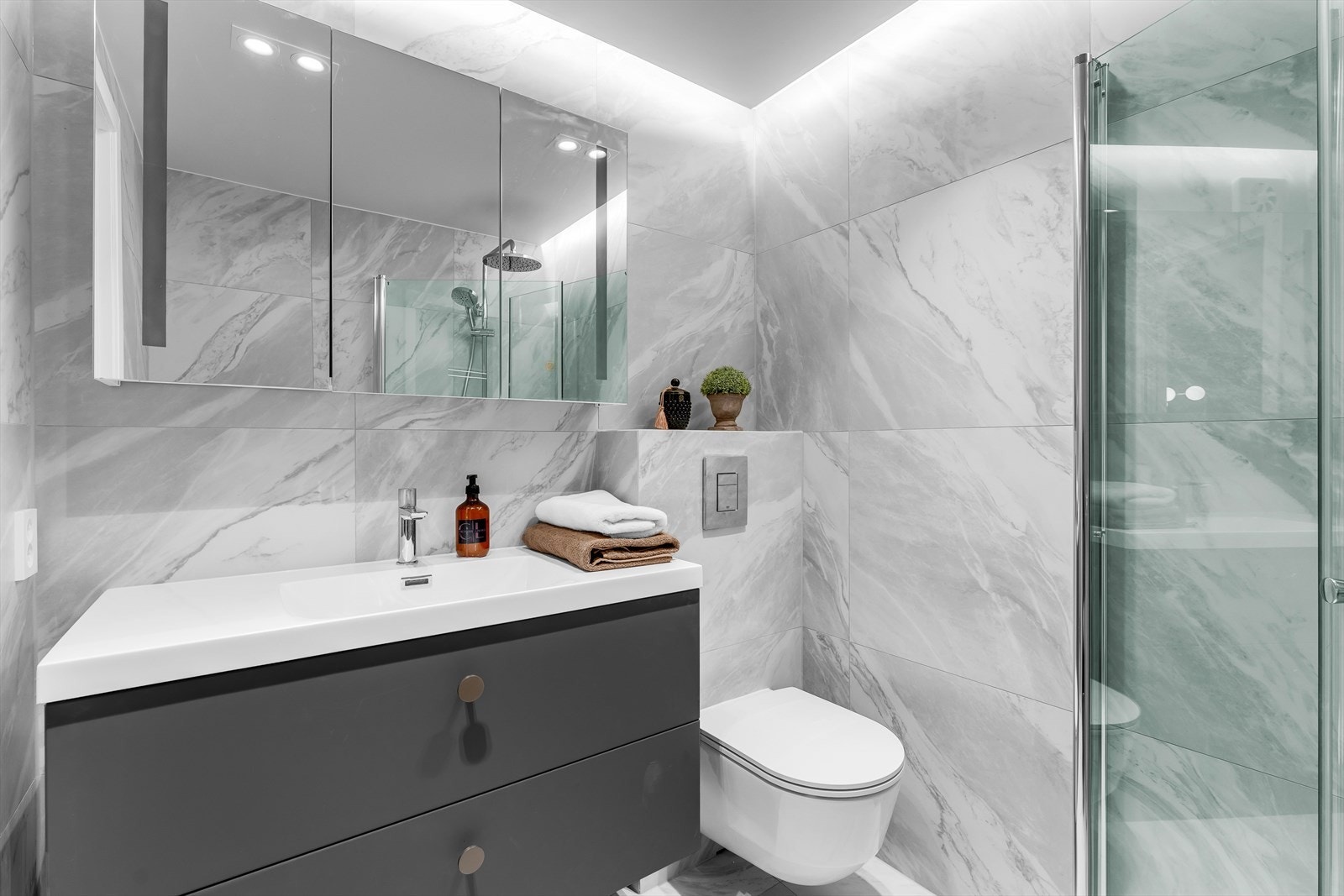 Badet inneholder speilskap med lys, baderomsinnredning med store skuffer og vegghengt wc med innebygget sisterne. Galleribilde