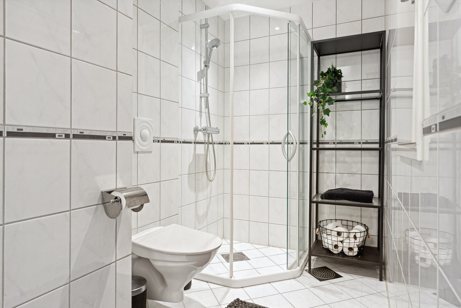 Dette badet er også flislagt og er utstyrt med vegghengt toalett, dusjhjørne og hvit baderomsinnredning Galleribilde
