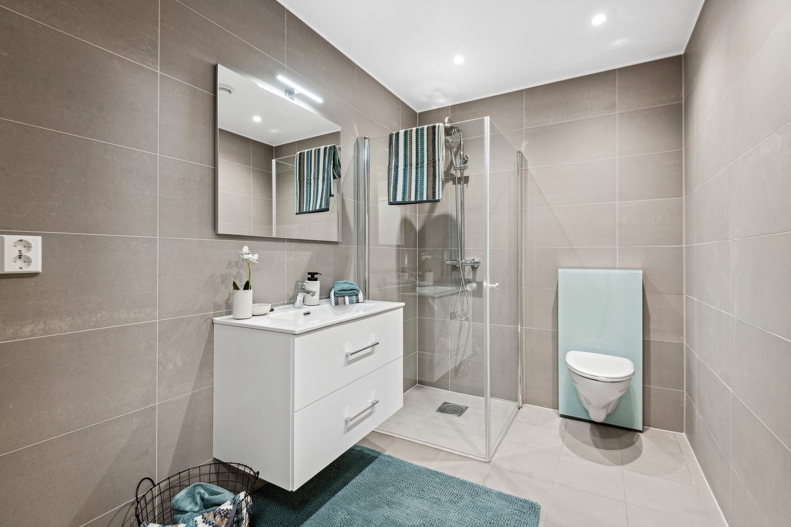 Bad oppgradert med downlights, skuffer under servanten, veggfestet toalett og flis i en lin farge både på vegg og gulv. Galleribilde