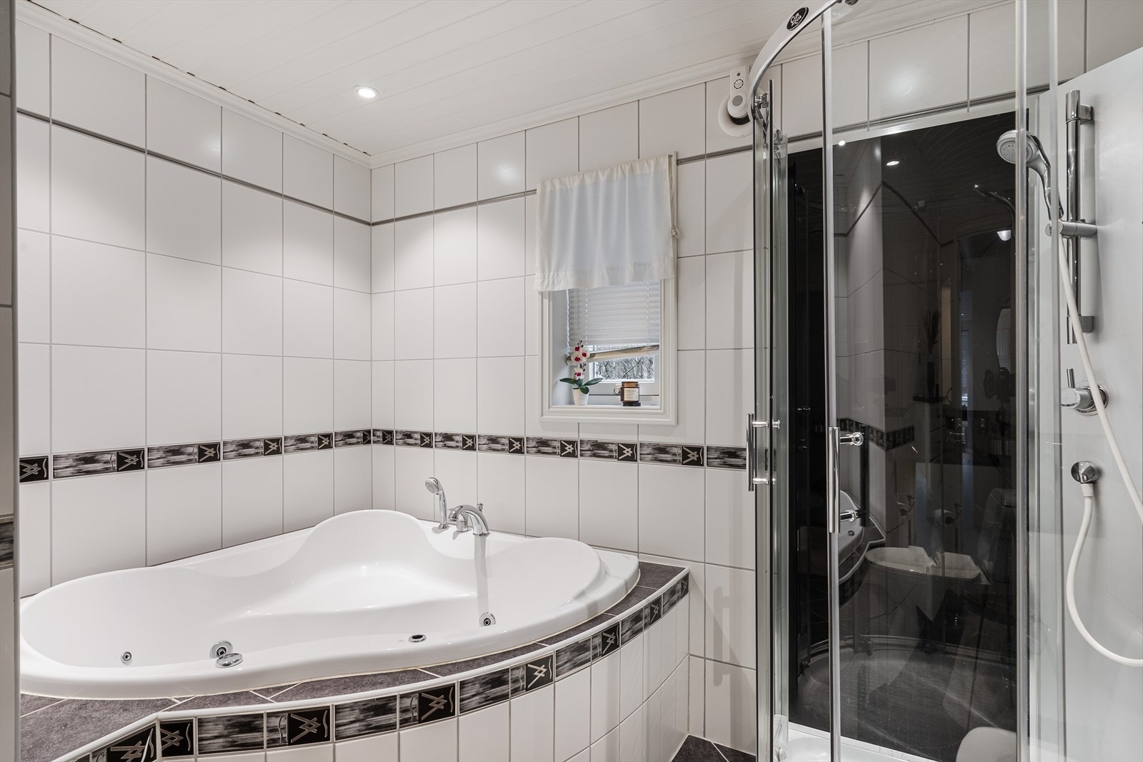 På badet er det montert toalett, badekar, dusjkabinett, mekanisk avtrekk og en hvit baderomsinnredning i over- og underskap med heldekkende servant, speil og belysning. Galleribilde