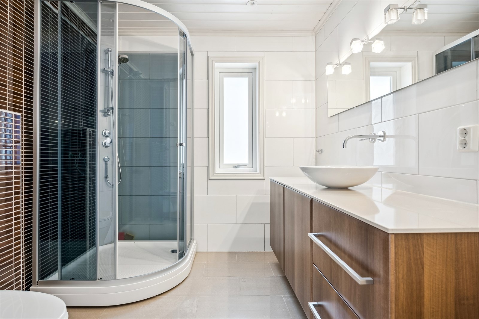 Badet i 1. etasje er innredet med en baderomsinnredning med toppmontert servant, speil med belysning, veggmontert toalett og dusjkabinett. Galleribilde