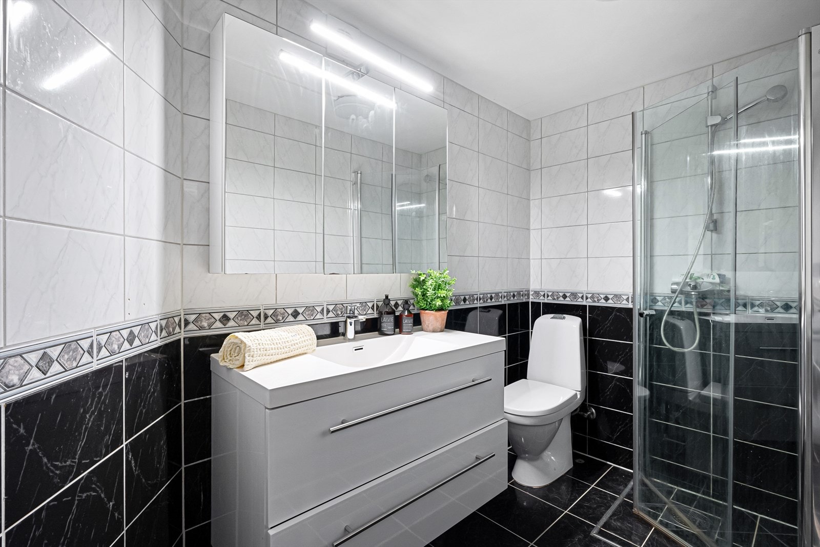 Badet har flislagte overflater, varmekabler i gulvet og inneholder toalett, dusj, innredning og opplegg for vaskemaskin. Galleribilde