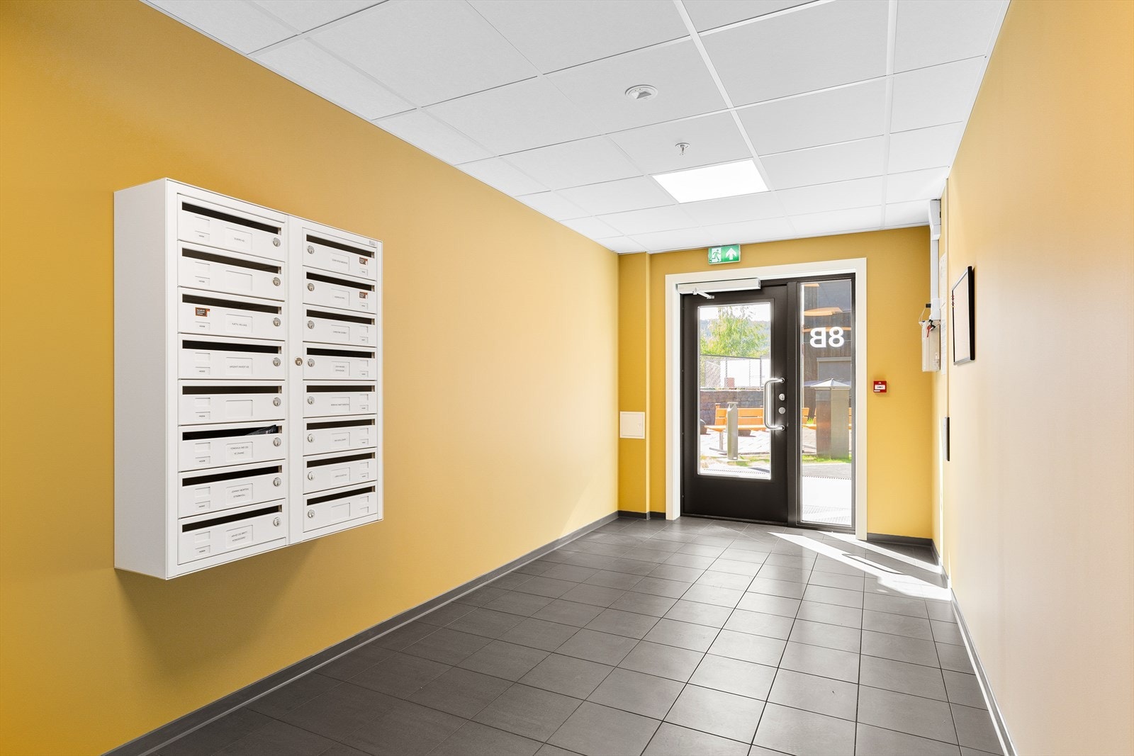 Felles innvendig trappegang, med blant annet postkasser og heis, og utgang til fellesarealet i midten. Galleribilde