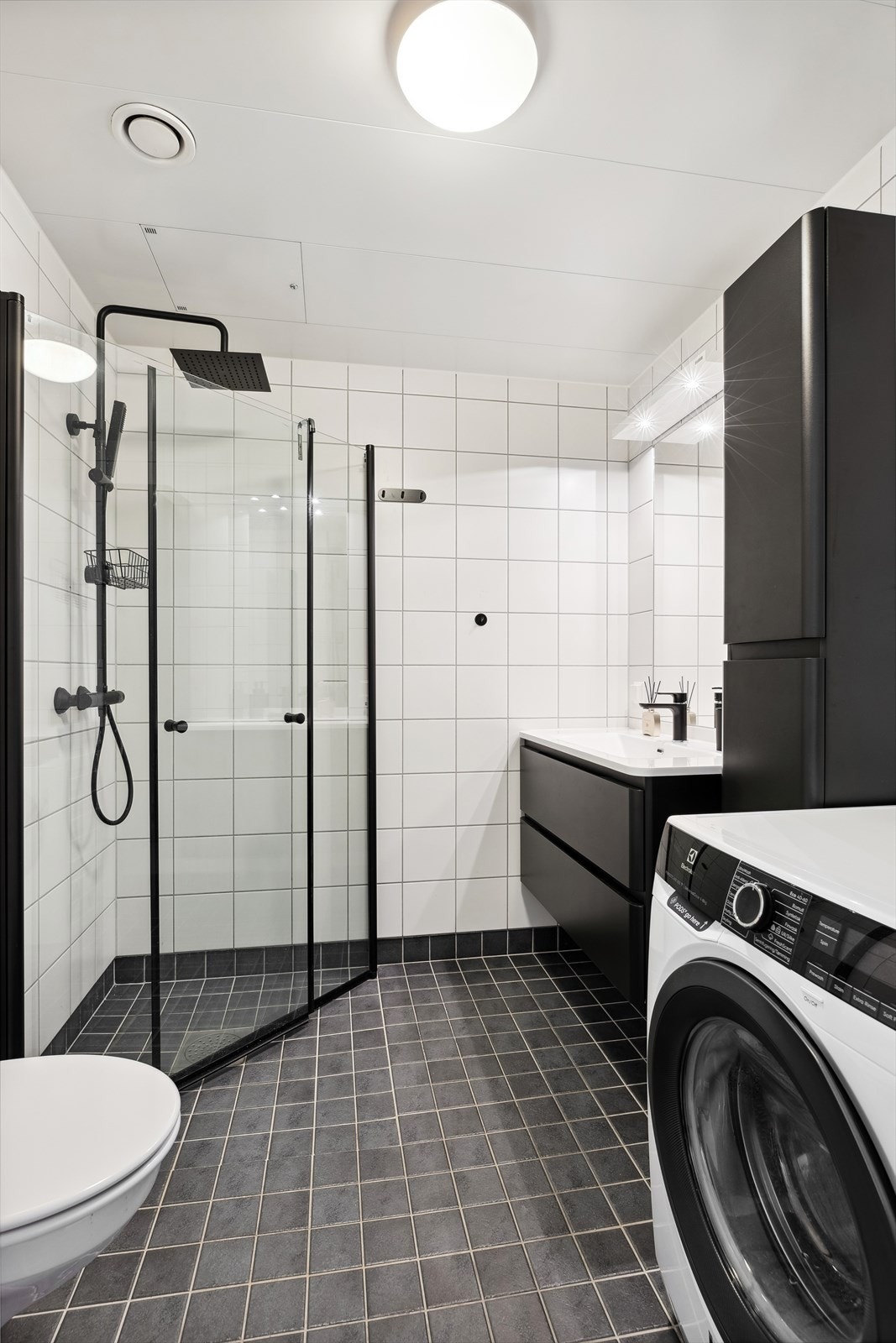 Badet har et tidløst utrykk, og har mørkt flislagt gulv med behagelig gulvvarme og lyse flislagte veggoverflater Galleribilde