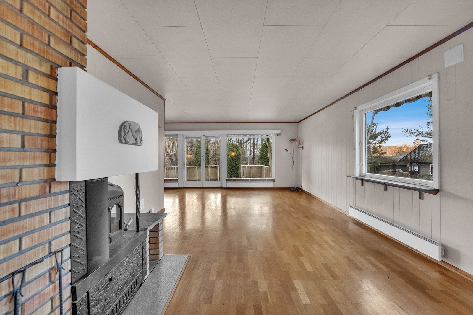 Det er peis i stuen, parkett på gulvet og veggene er kledd med malt panel. Galleribilde