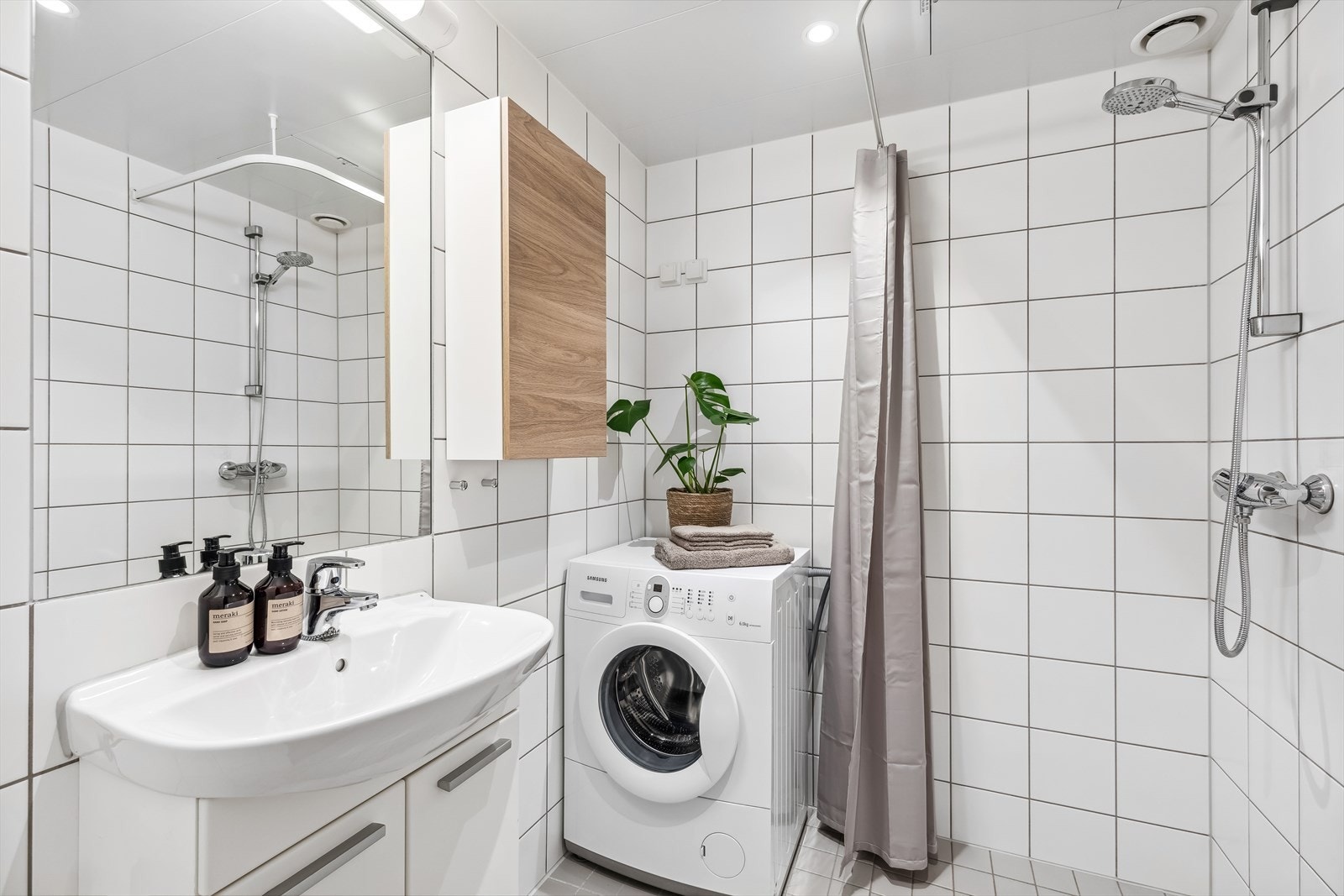 Badet er utstyrt med vegghengt klosett, servant, innfliset speil med overlys, veggskap og åpen dusj med forheng Galleribilde