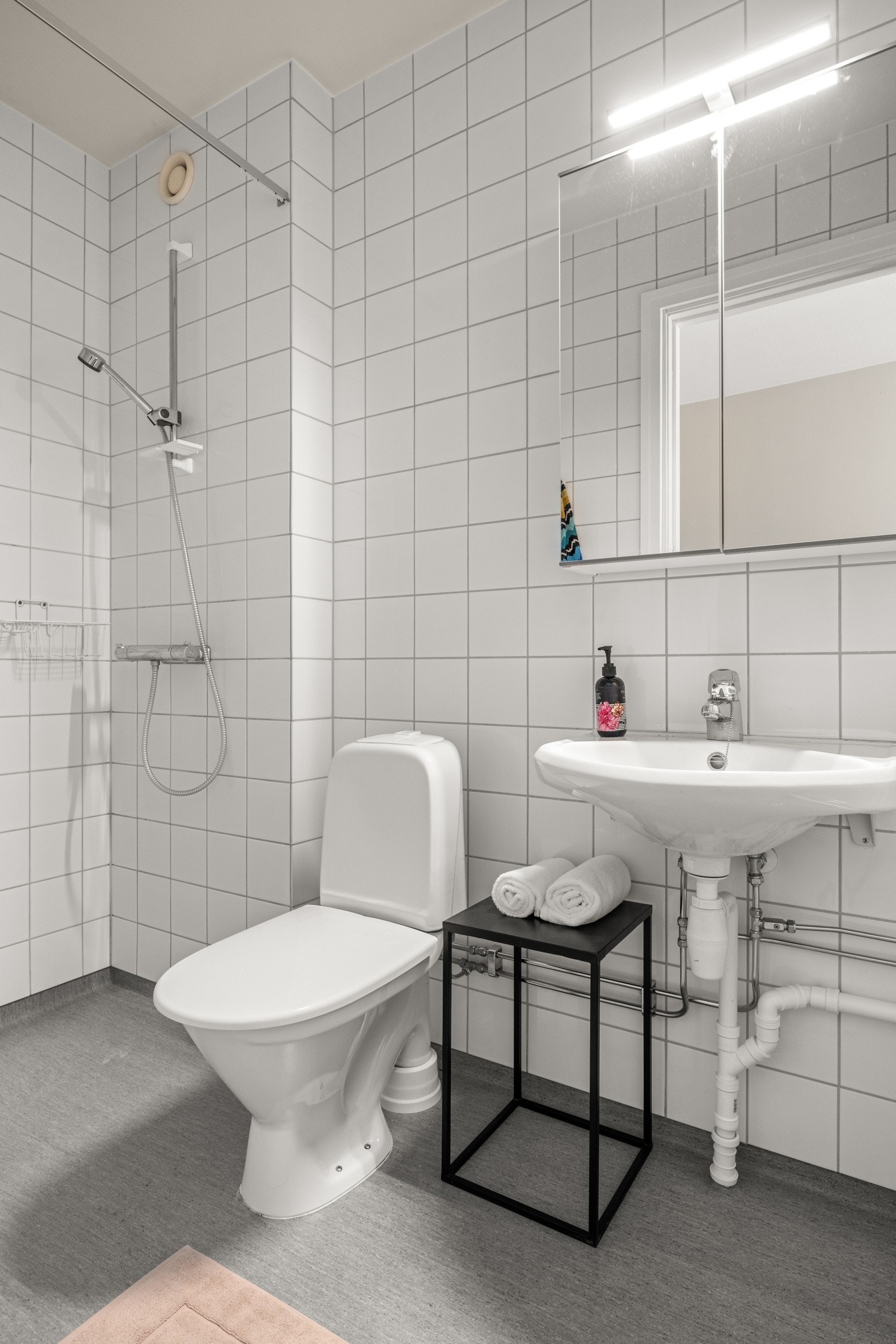 Bad/wc med romslig dusjhørne, vegghengt servant og speilskap med integrert belysning. Flislagte vegger og malt himling. Gulvet har vinylbelegg. Radiator tilkoblet fjernvarme på bad/wc. Galleribilde