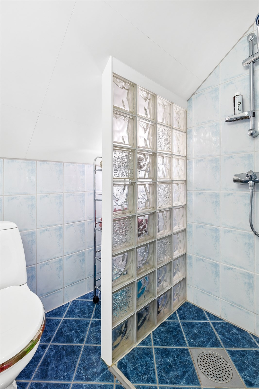 Badet er innredet med dusjnisje med vegg av glassbyggerstein og innfellbar glassdør, frittstående toalett og servantskap med profilerte fronter med heldekkende porselensservant. Overhengende speil med belysning Galleribilde