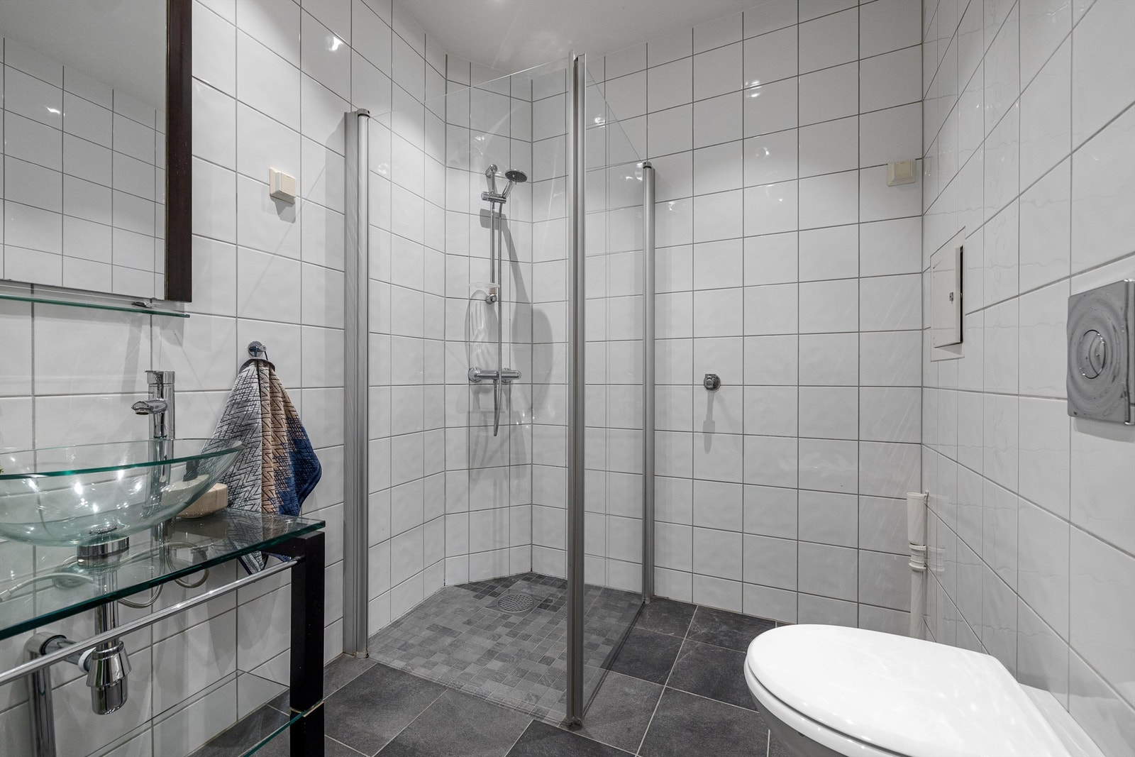 Servant i glass på skapinnredning med speil over, samt dusjhjørne med dører i glass. Opplegg til vaskemaskin. Galleribilde