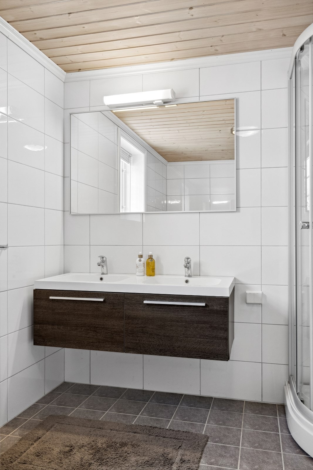 Badet ligger i 2. etasje og er innredet med et dusjkabinett, veggmontert toalett, delikat innredning med dobbel heldekkende servant og speil med overliggende belysning. Galleribilde