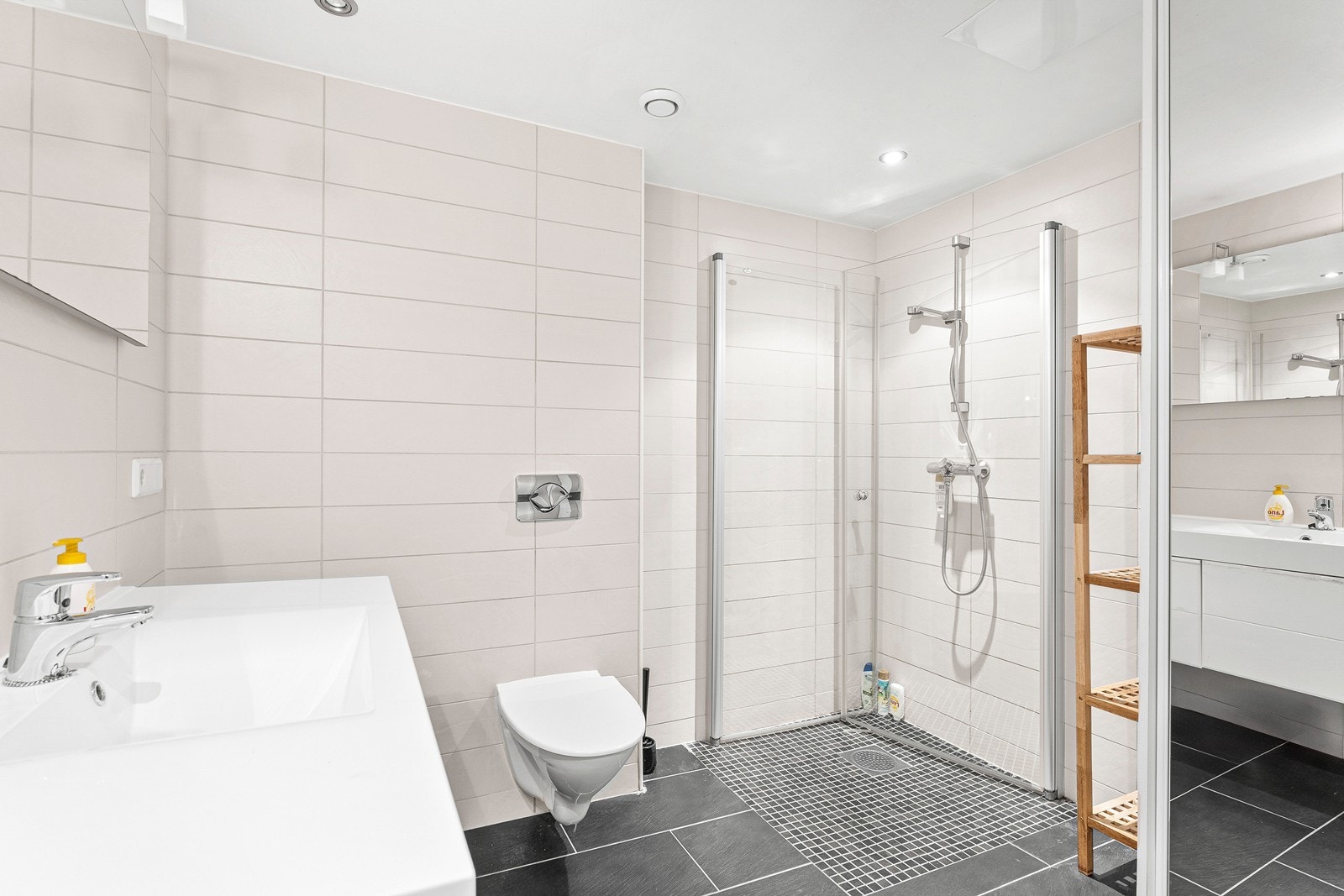 Badet er utstyrt med dusjhjørne med svingdører i glass, vegghengt toalett, servantskap og høyskap. Galleribilde