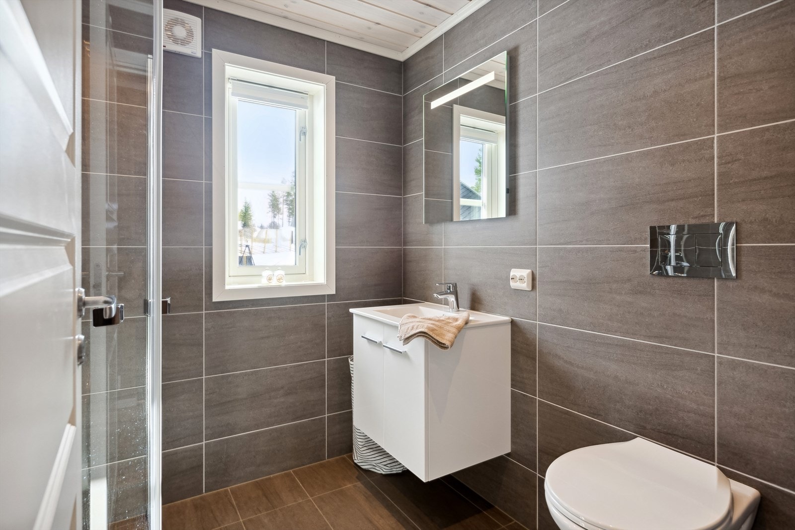 Badet har flislagte overflater, og har vegghengt toalett, dusj og baderomsinnredning med servant. Galleribilde