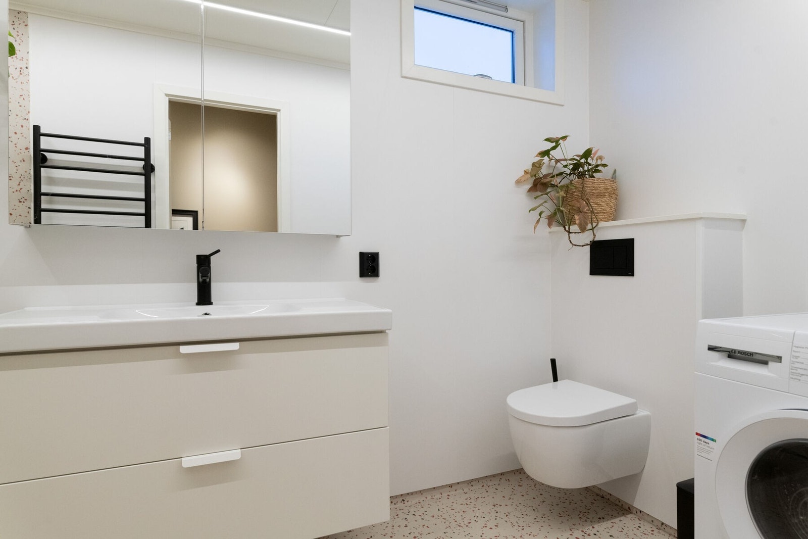 Badet har vegghengt wc, servant på innredning, dusjhjørne og opplegg for vaskemaskin. Galleribilde