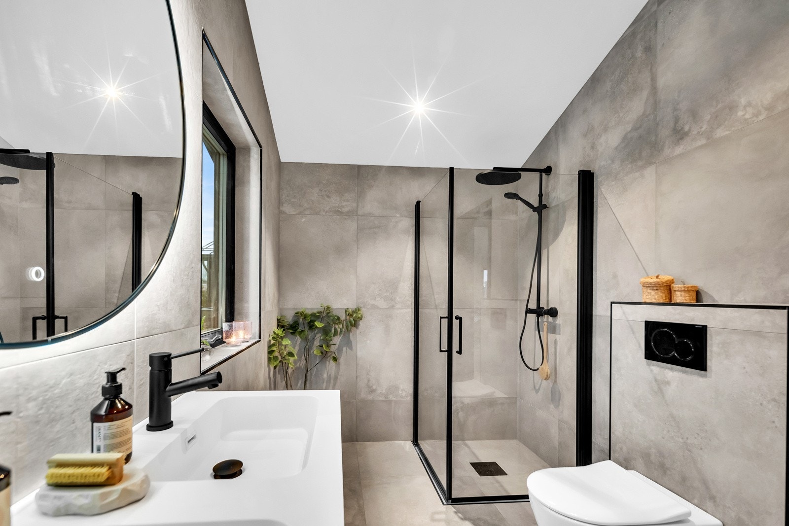 På badet ved hovedsoverom er det et rundt speil med bakenforliggende belysning og en stilig, sort skuffeinnredning med dobbel servant. Galleribilde