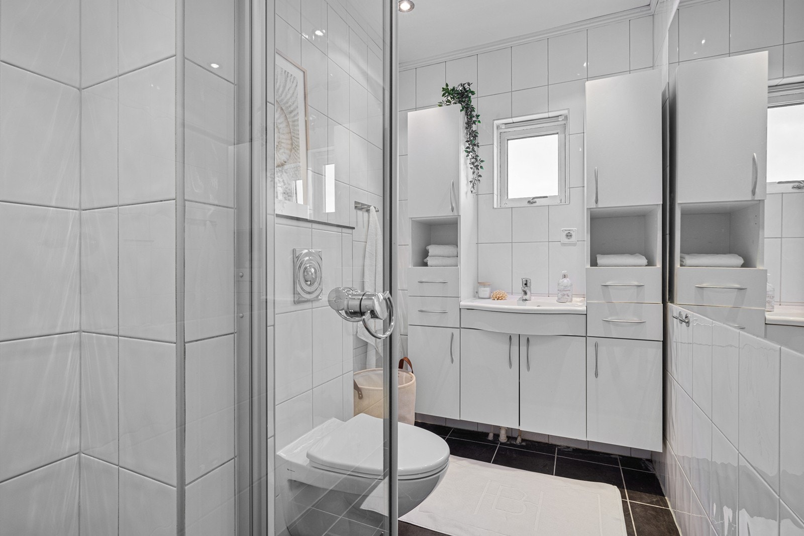 Badet har flislagt gulv med varmekabler, flislagte vegger, vannklosett, dusjnisje, servant og baderomsinnredning. Galleribilde