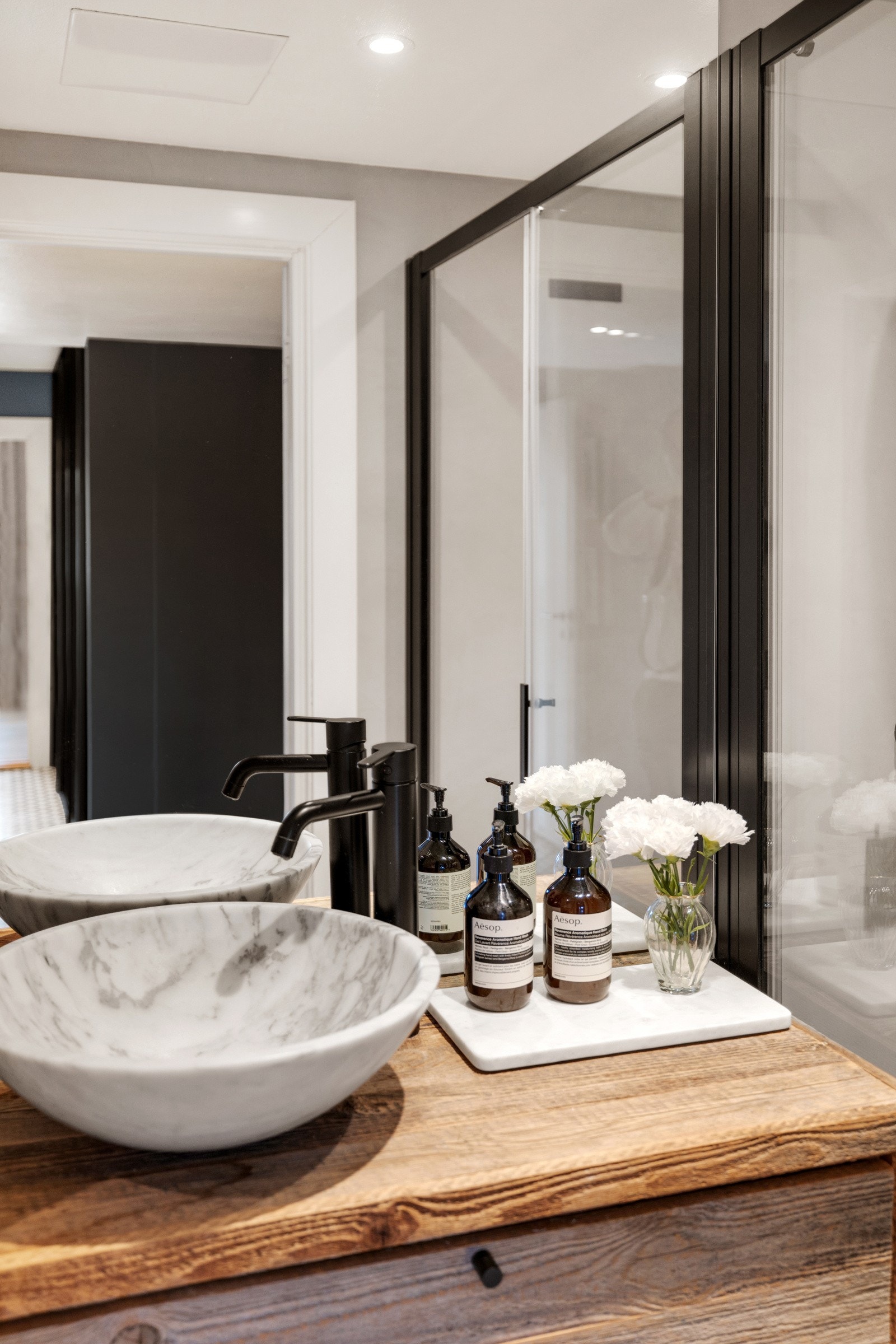 Badet har et stilfullt preg med lyse fliser, lys marmor bolleservant og sorte detaljer som står i perfekt kombinasjon til hverandre. Galleribilde