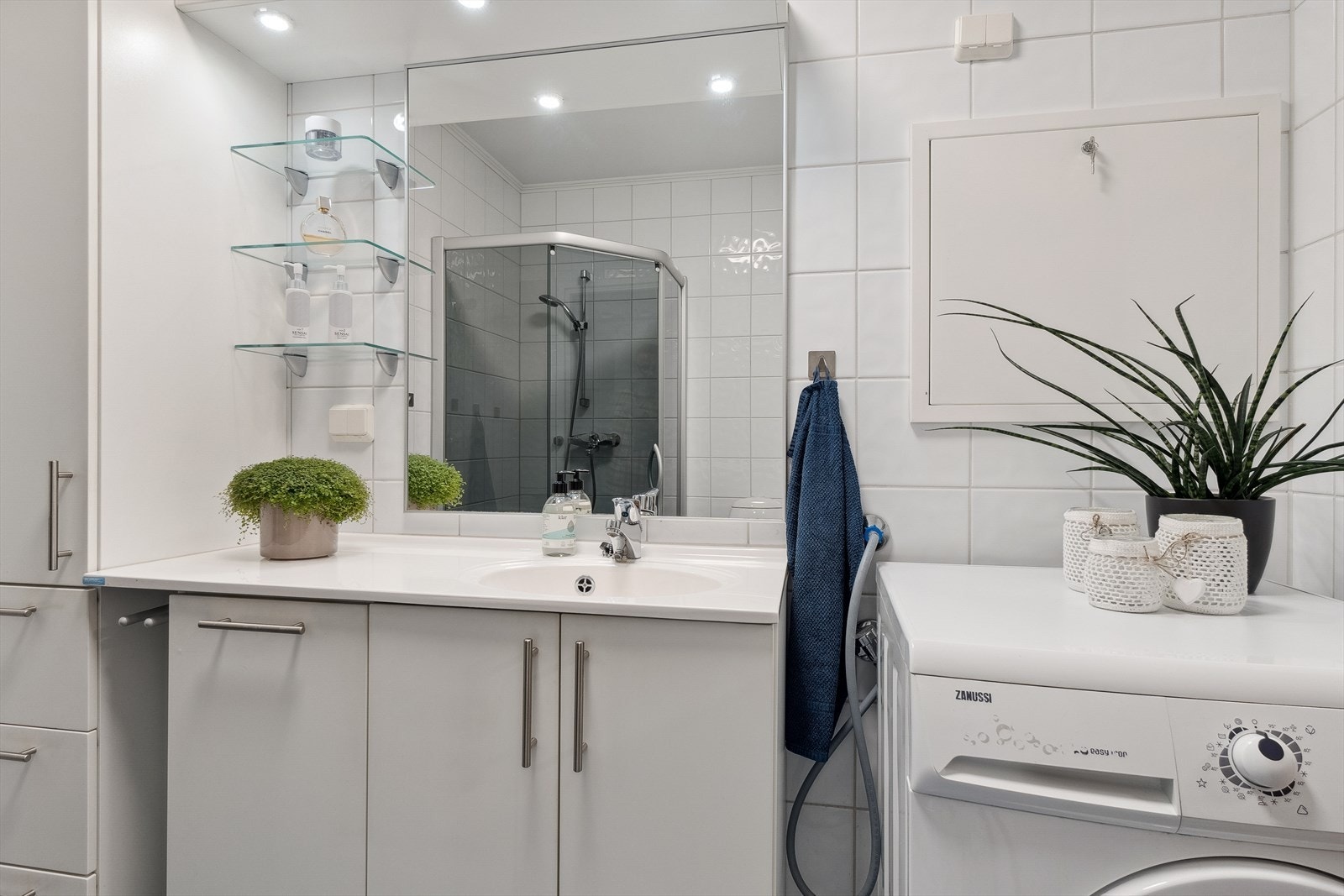 Heldekkende servant, høyskap og speil på vegg med lys over. Dusjhjørne med glassvegger og opplegg for vaskemaskin. Galleribilde