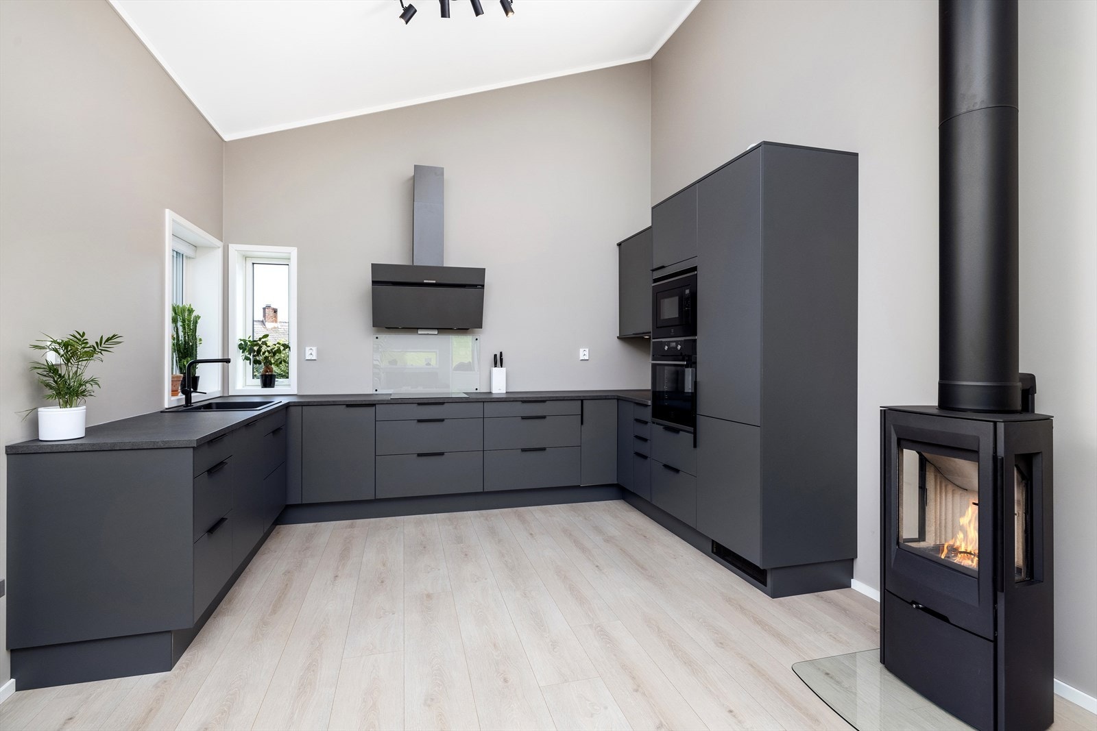 Mørkegrå og toppmoderne kjøkkeninnredning fra Norema, med slette fronter, laminat benkeplate og integrerte hvitevarer, samt peisovn med stålpipe. Galleribilde