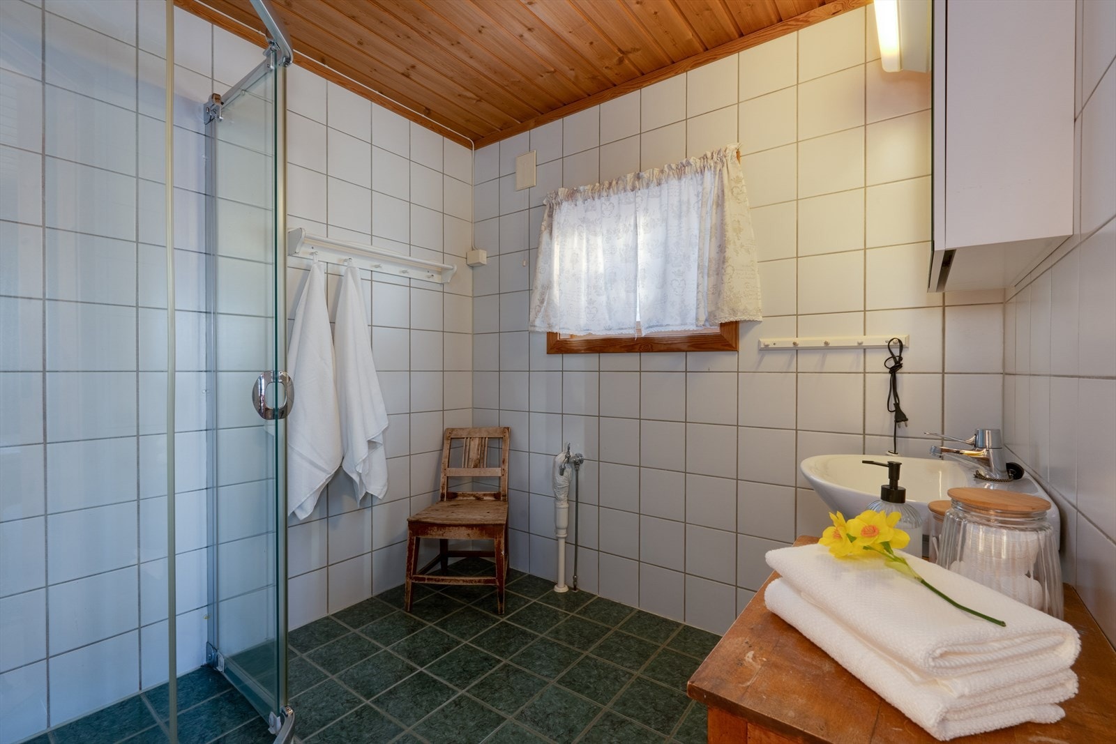 Baderommet er innredet med helflisede overflater på vegger og gulv.
Det er etablert dusjhjørne, vaskeservant med overskap, og uttak for vaskemaskin. Galleribilde