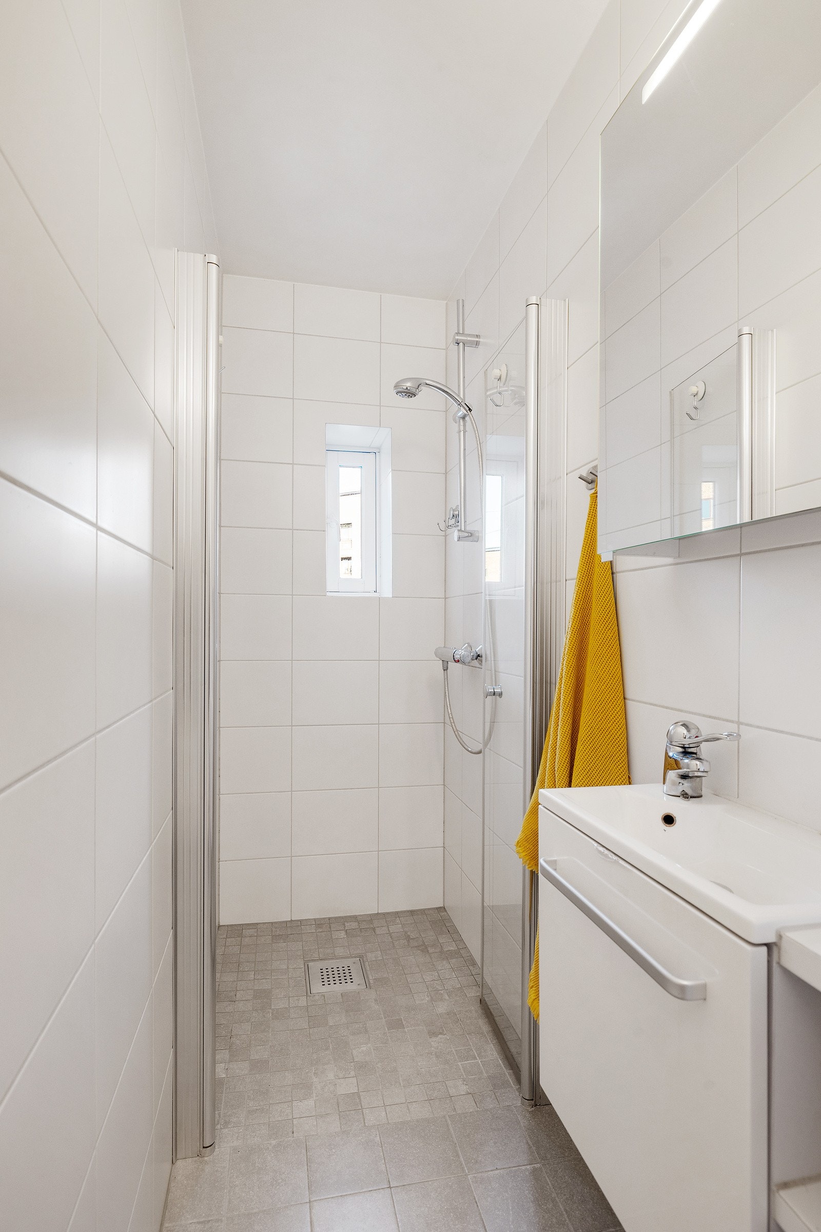 Badet inneholder vegghengt innredning med heldekkende servant, speilskap med belysning, gulvmontert toalett og dusjnisje. Galleribilde
