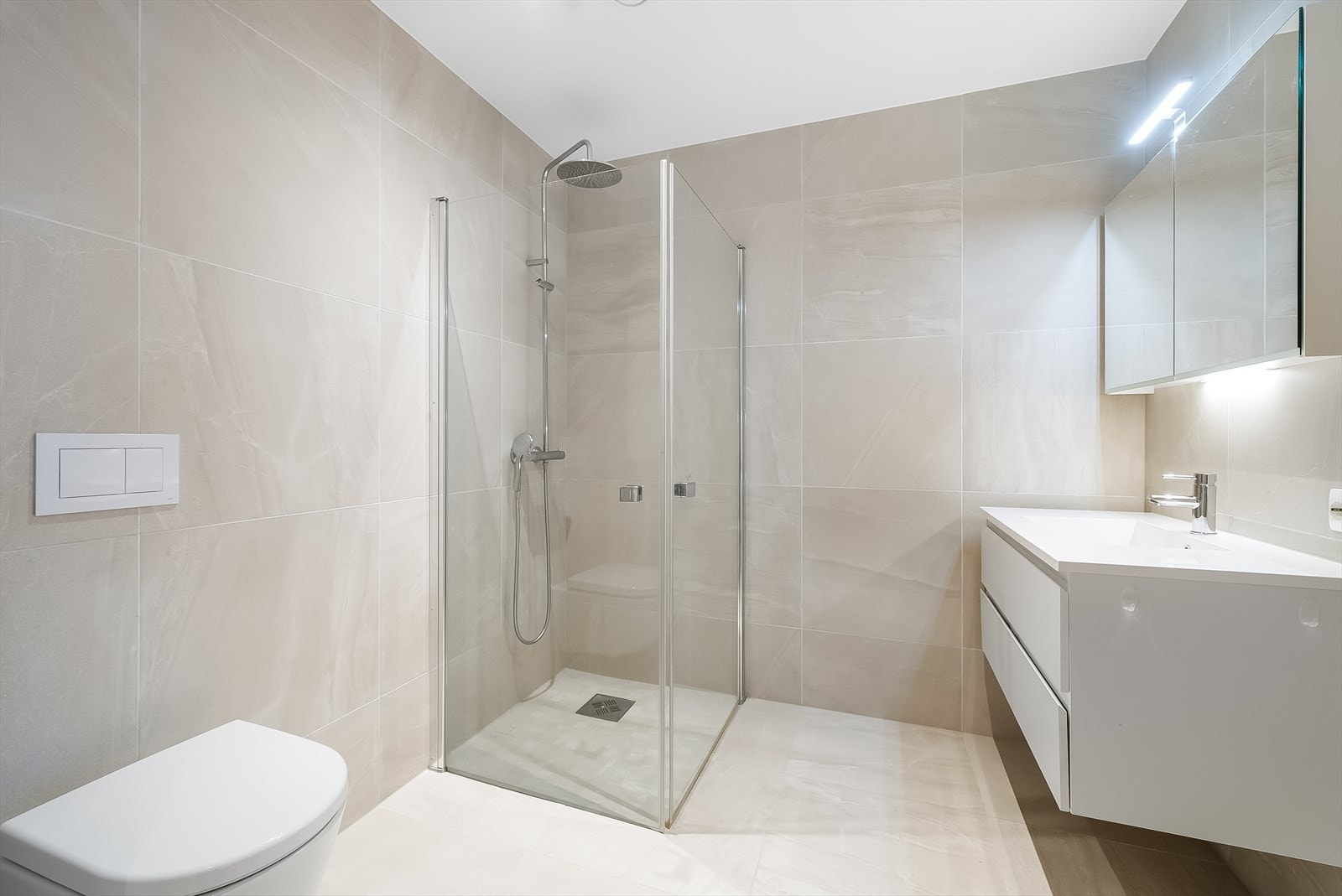 Tidløst og delikat utformet bad med fliser på gulv og vegger. Badet er innredet med baderomsinnredning, toalett og dusjløsning. Galleribilde