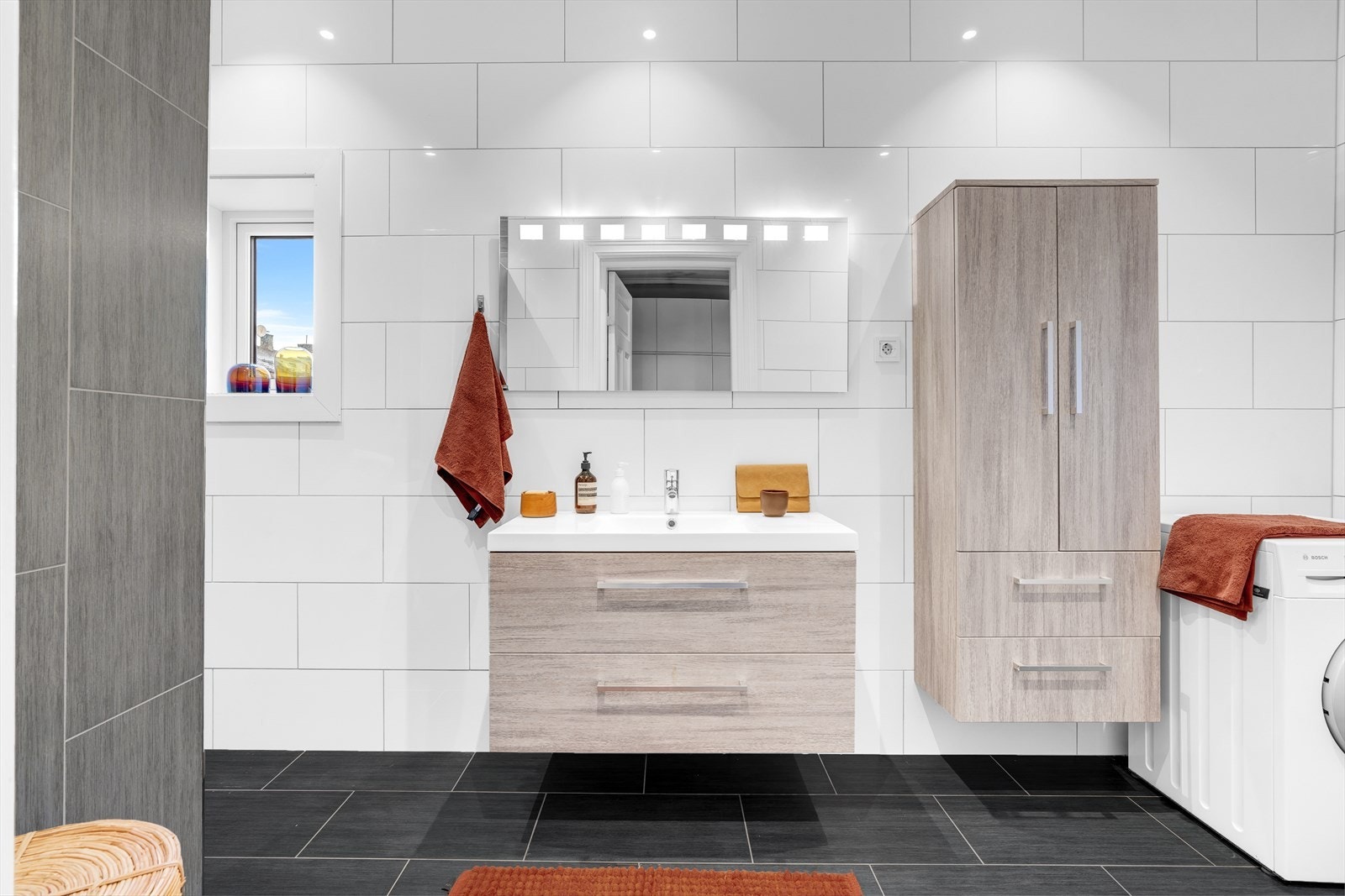 Baderommet er utstyrt med servant med innredning, speil, veggskap, opplegg for vaskemaskin, vegghengt toalett og dusjnisje Galleribilde