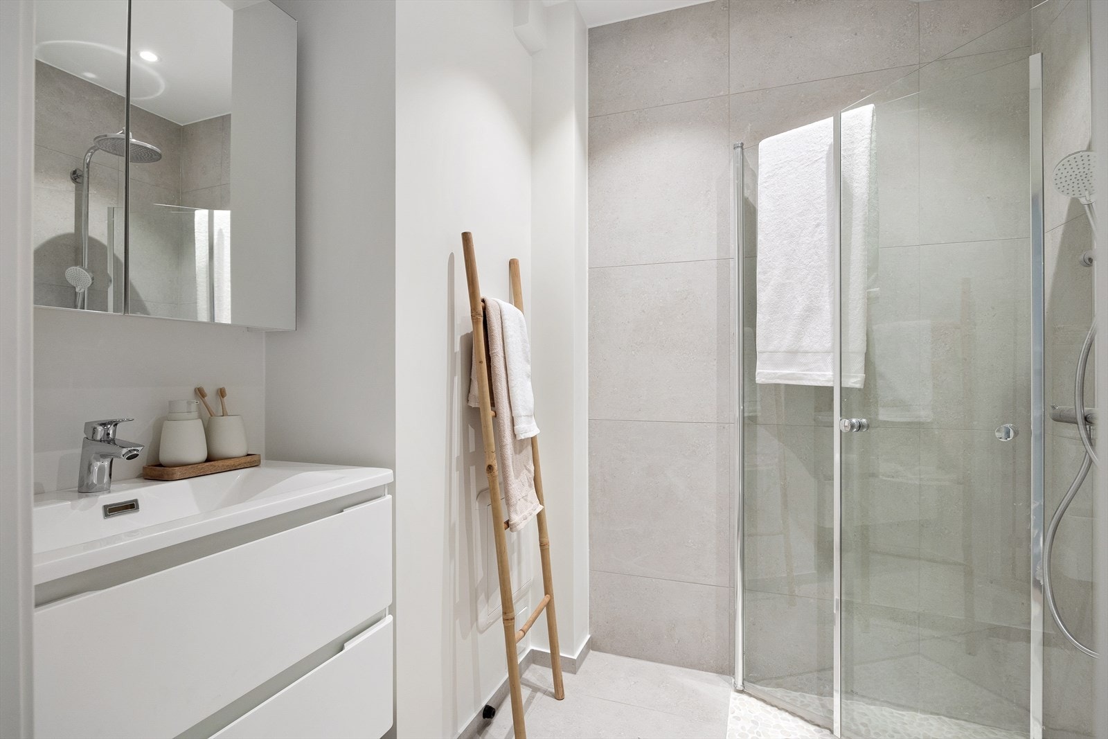 Badet er innredet med vegghengt klosett, servant nedfelt i innredning, speilskap og dusjhjørne med svingbare glassdører. Det er naturstein i dusjsonen. Galleribilde