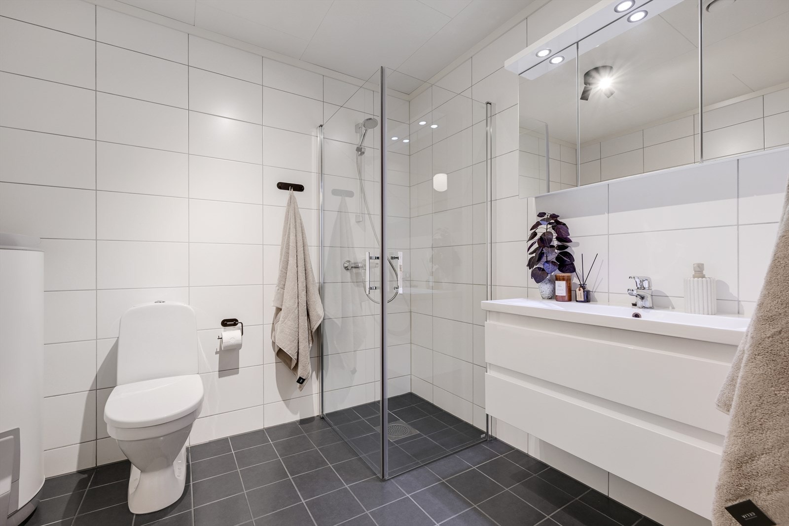 Fliselagt bad/wc med varmekabler, dusjhjørne, wc, servant med skuffer og speilskap. Galleribilde