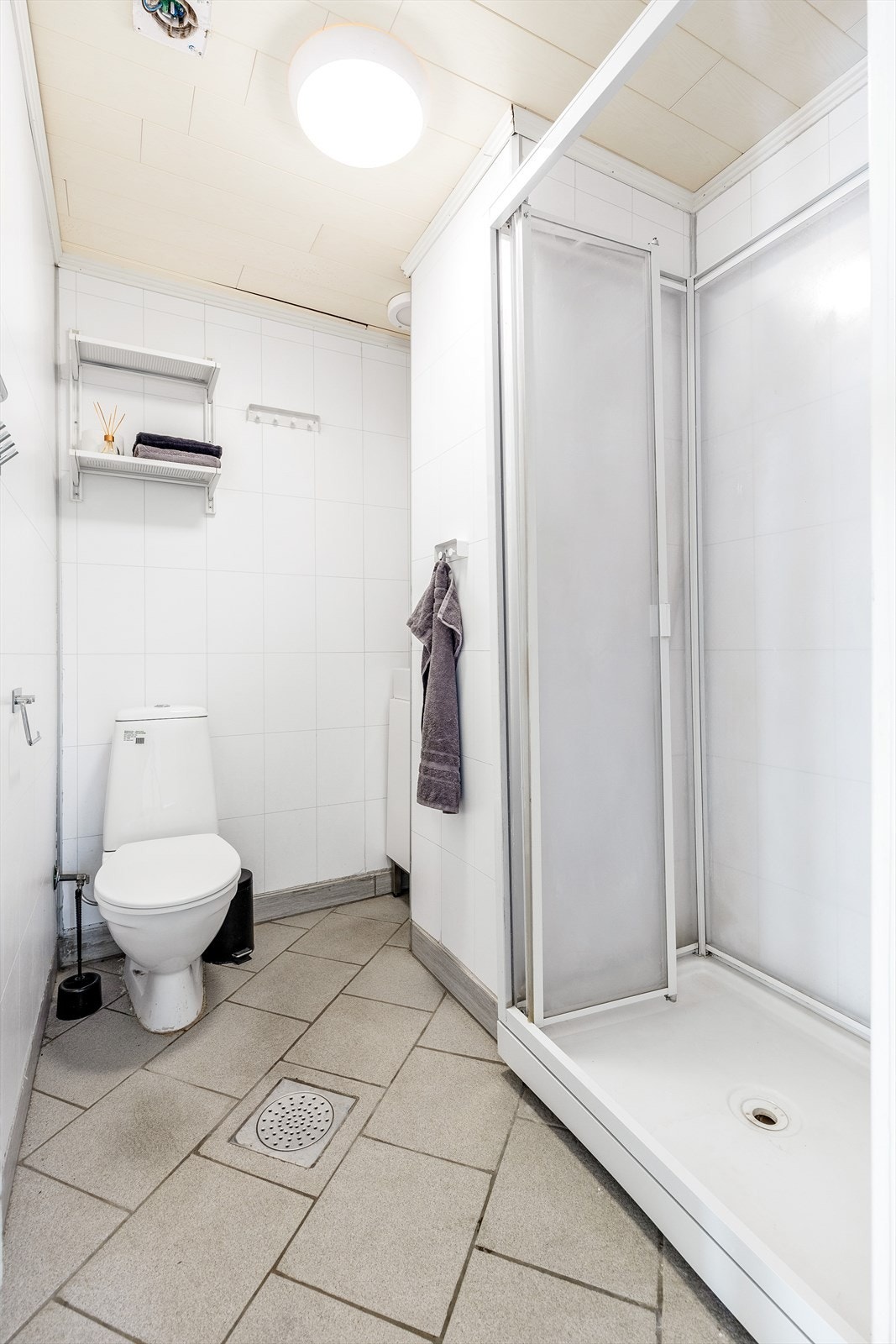 Lyst flislagt bad med varmekabler i gulv. Badet er innredet med liten servantinnredning, speilskap, toalett og dusjkabinett. Galleribilde