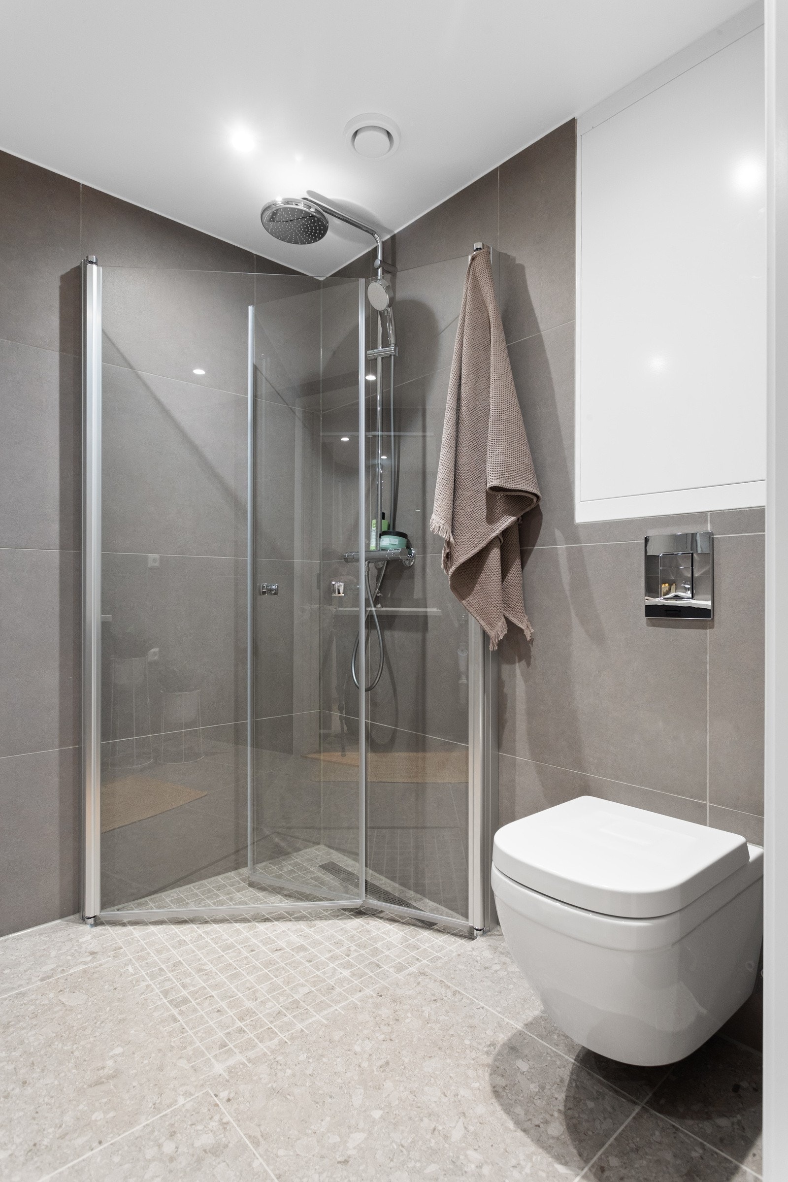 Nedsenket dusjsone med mosaikkfliser på gulv, innfellbare glassdører og både hånd- og regnfallsdusj. Baderommet er også utstyrt med vegghengt toalett med soft-close toalettsete. Galleribilde