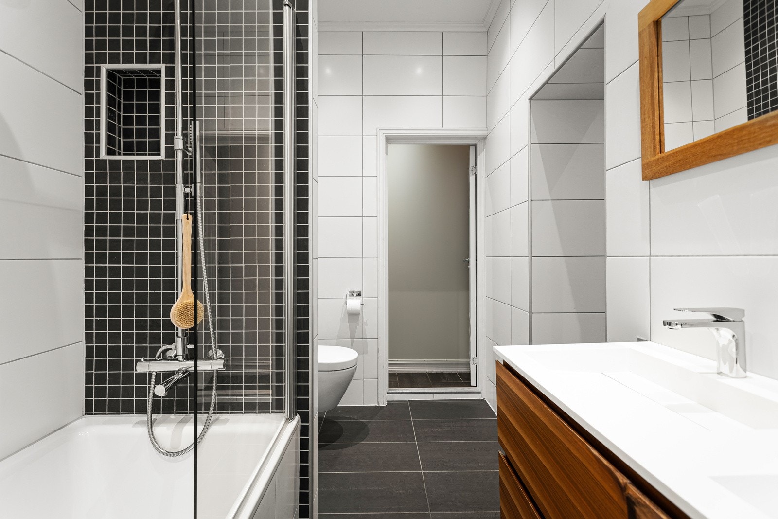 Badet har innfliset badekar, dusjgarnityr med regnfalls- og håndholdt dusj og veggmontert klosett med innfliset sisterne Galleribilde