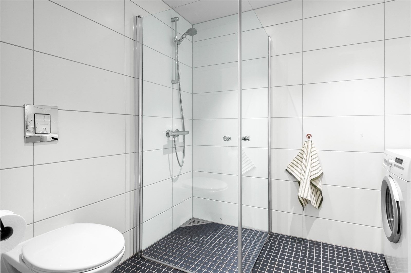 Badet er utstyrt med romslig dusjhjørne, vegghengt toalett, samt god plass til vaskemaskin og tørketrommel. Galleribilde