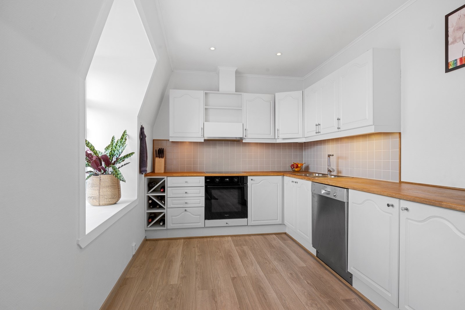 Tidløst og funksjonell kjøkkeninnredning med lyse, profilerte fronter og benkeplate i tre med fliser på veggen over Galleribilde