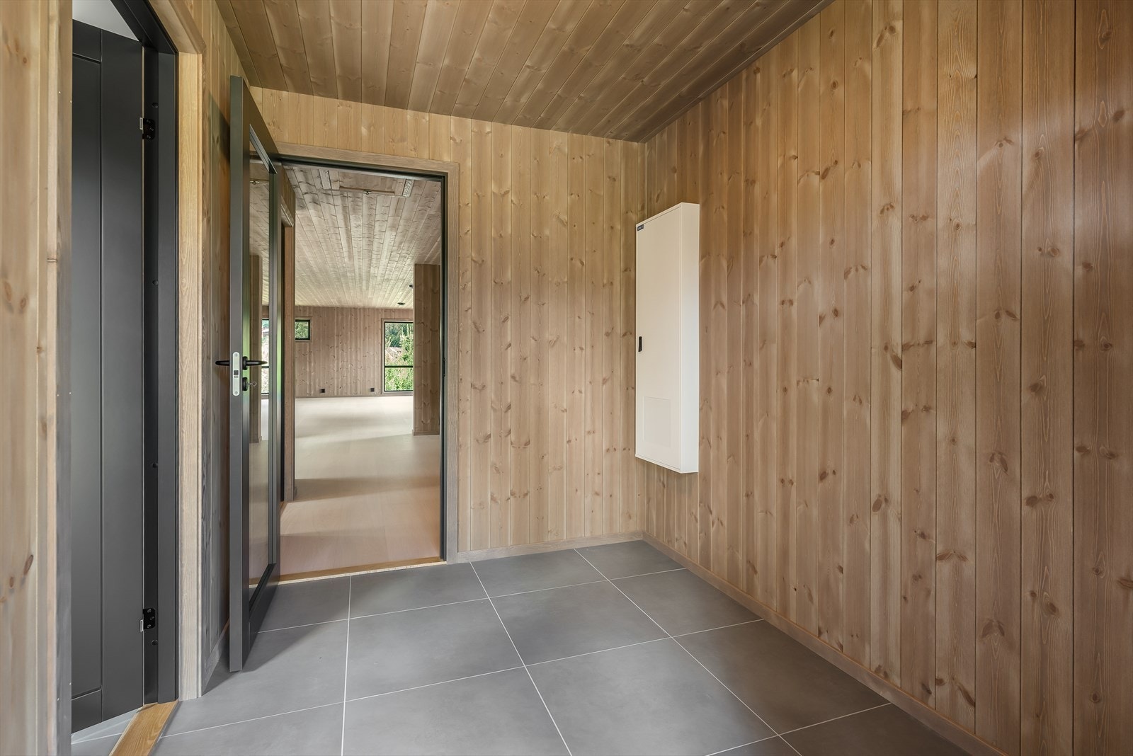 En fin entré ønsker deg velkommen inn. Her er det flislagt gulv, beiset panel på vegger og i himling.
God plass for å etablere oppbevaringsløsninger for sko og yttertøy om ønskelig. Galleribilde