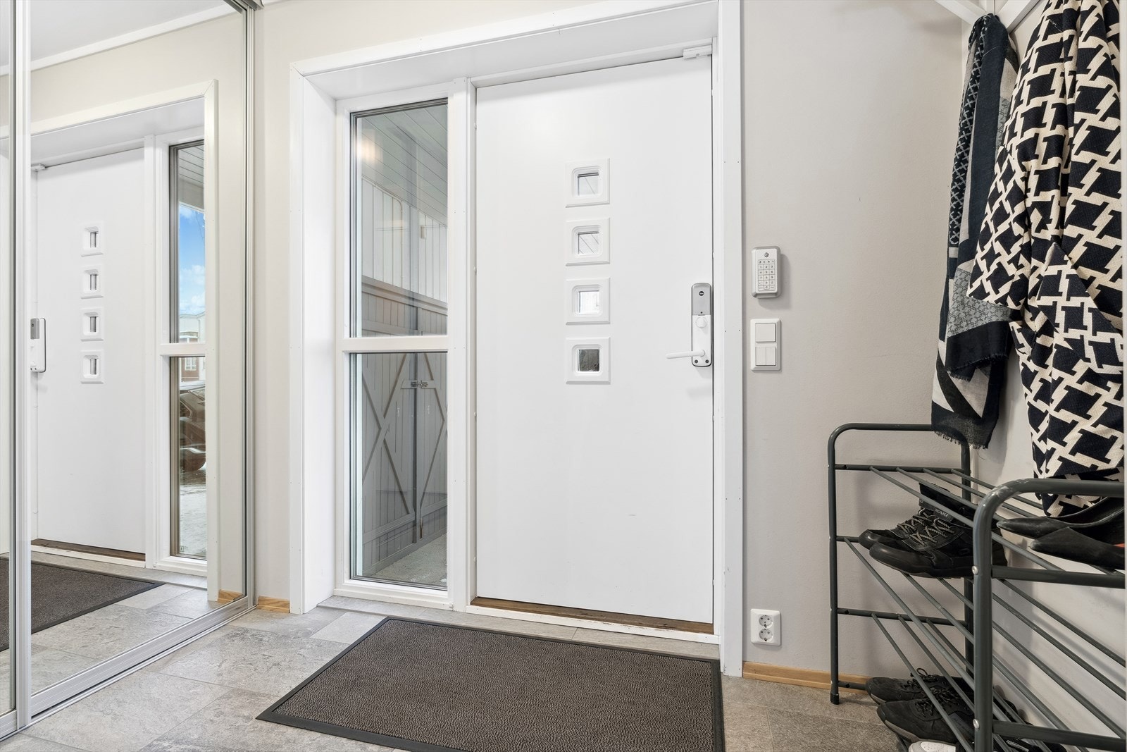 Entréen oppleves som romslig og lun. Flislagt gulv med varme. Skyvedørsgarderobe med speilfronter samt god plass til å henge fra seg yttertøy og parkere sko. Dør med kodelås. Alarmsystem fra Verisure kan overdras til kjøper. Galleribilde
