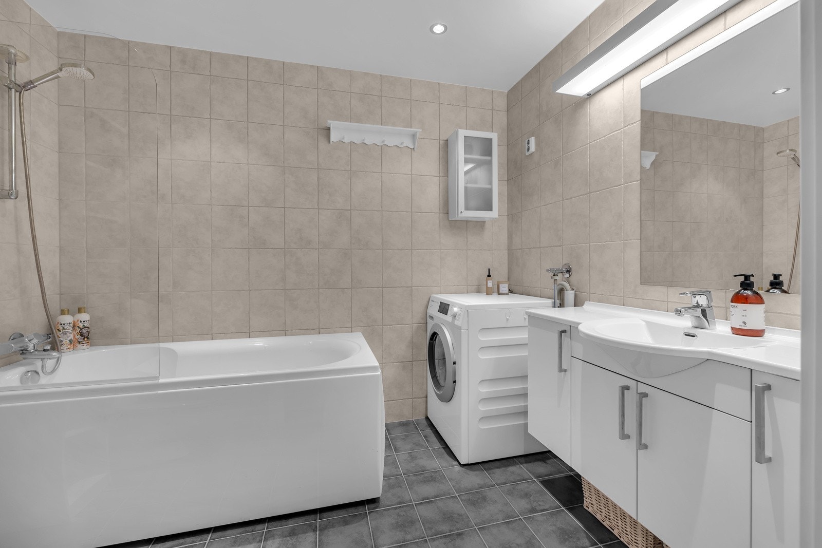 Her er det opplegg for vaskemaskin og tørketrommel, en praktisk innredning med god oppbevaringsplass og badekar Galleribilde
