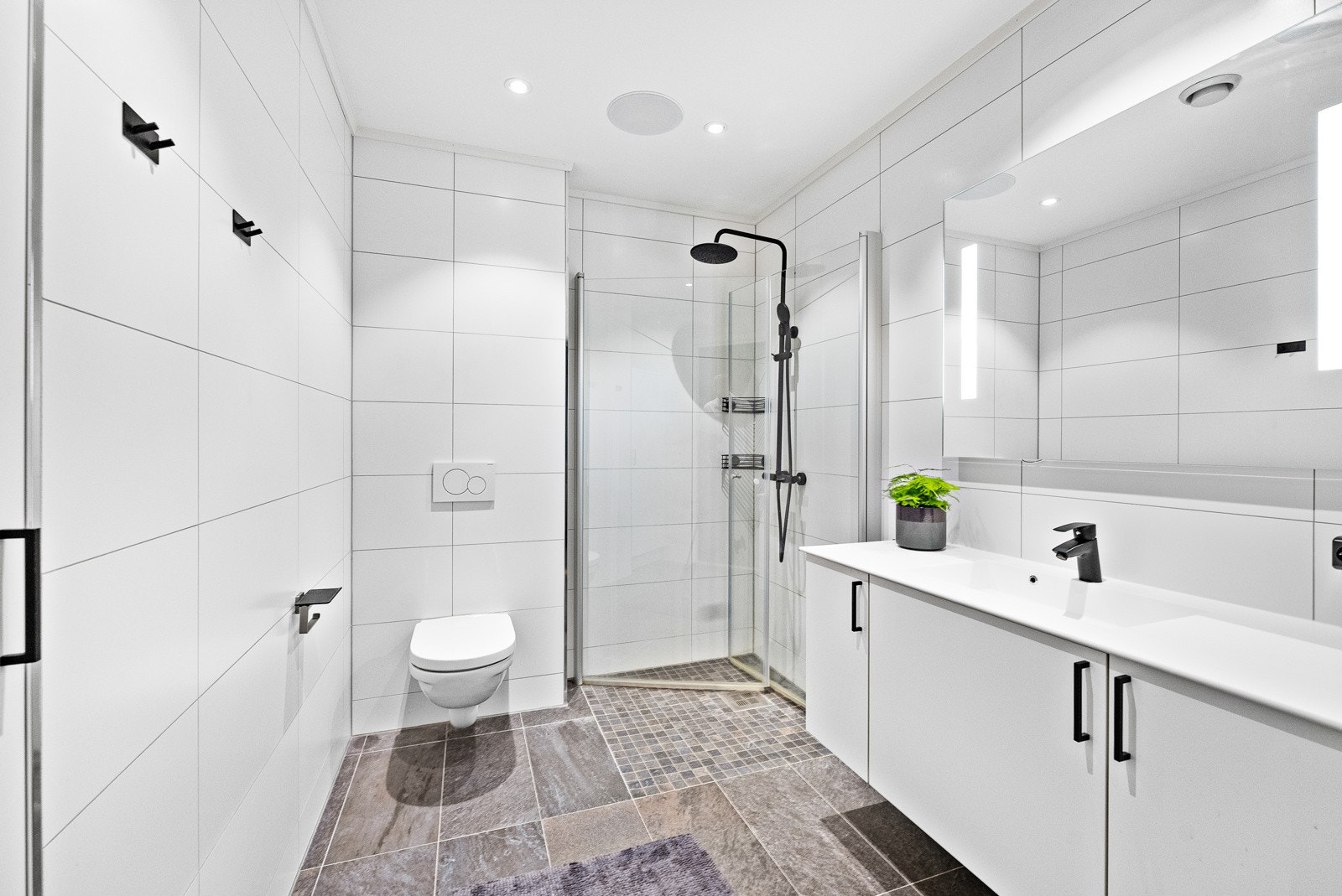 Meget stilrent baderom med flislagt gulv med gulvvarme og flislagte vegger, med nedsenket himling med downlights Galleribilde