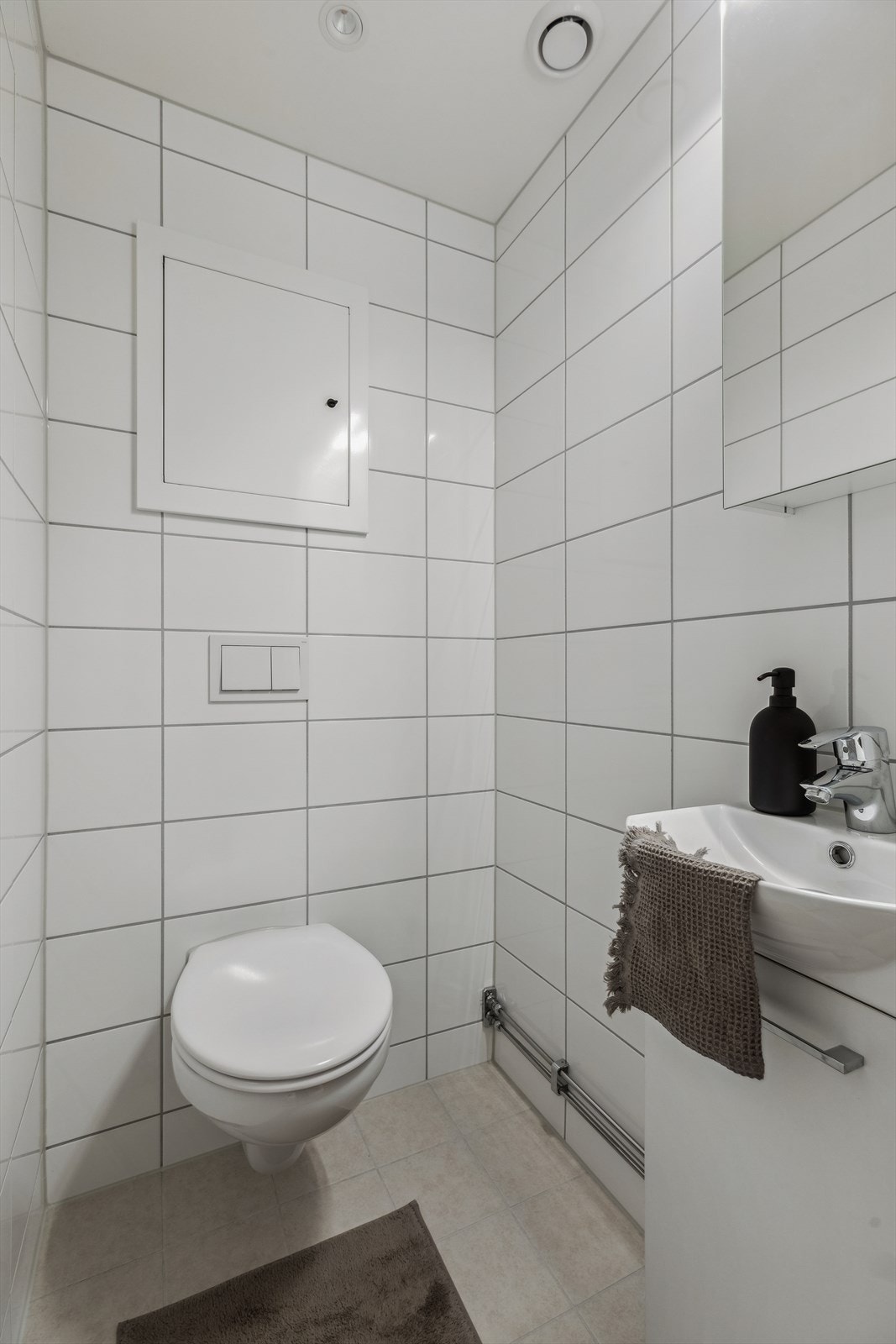 Det er fliser på vegger og gulv med varmekabler. Servant med servantskap og veggfestet toalett med skjult sisterne Galleribilde