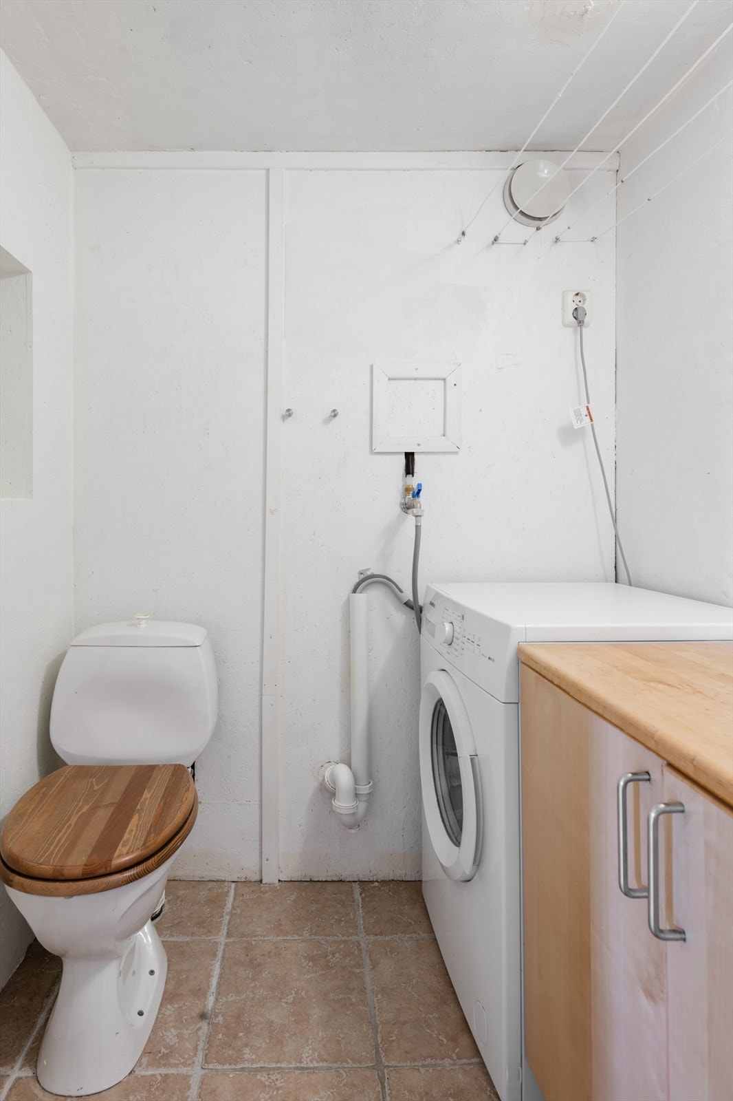 Fliser på gulv og malt murvegger. Opplegg for vaskemaskin. Benk med servant og skap under. Galleribilde