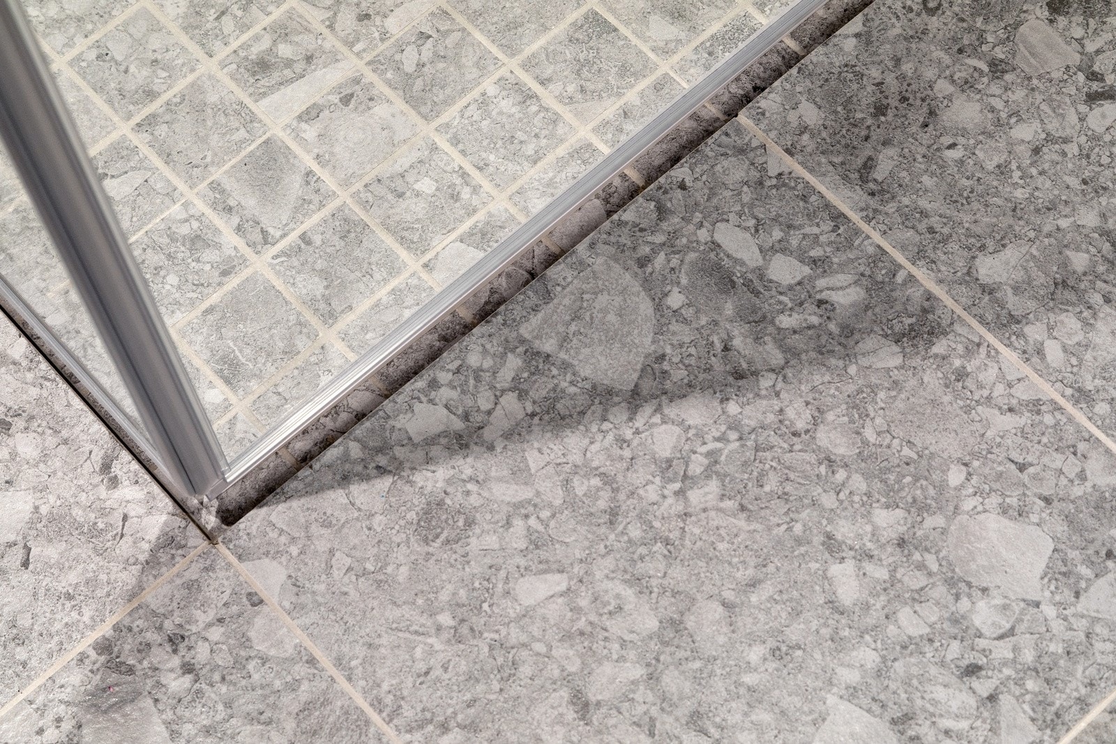 Nedsenket dusjsone med mosaikkfliser på gulv, innfellbare glassdører og både hånd- og regnfallsdusj. Galleribilde