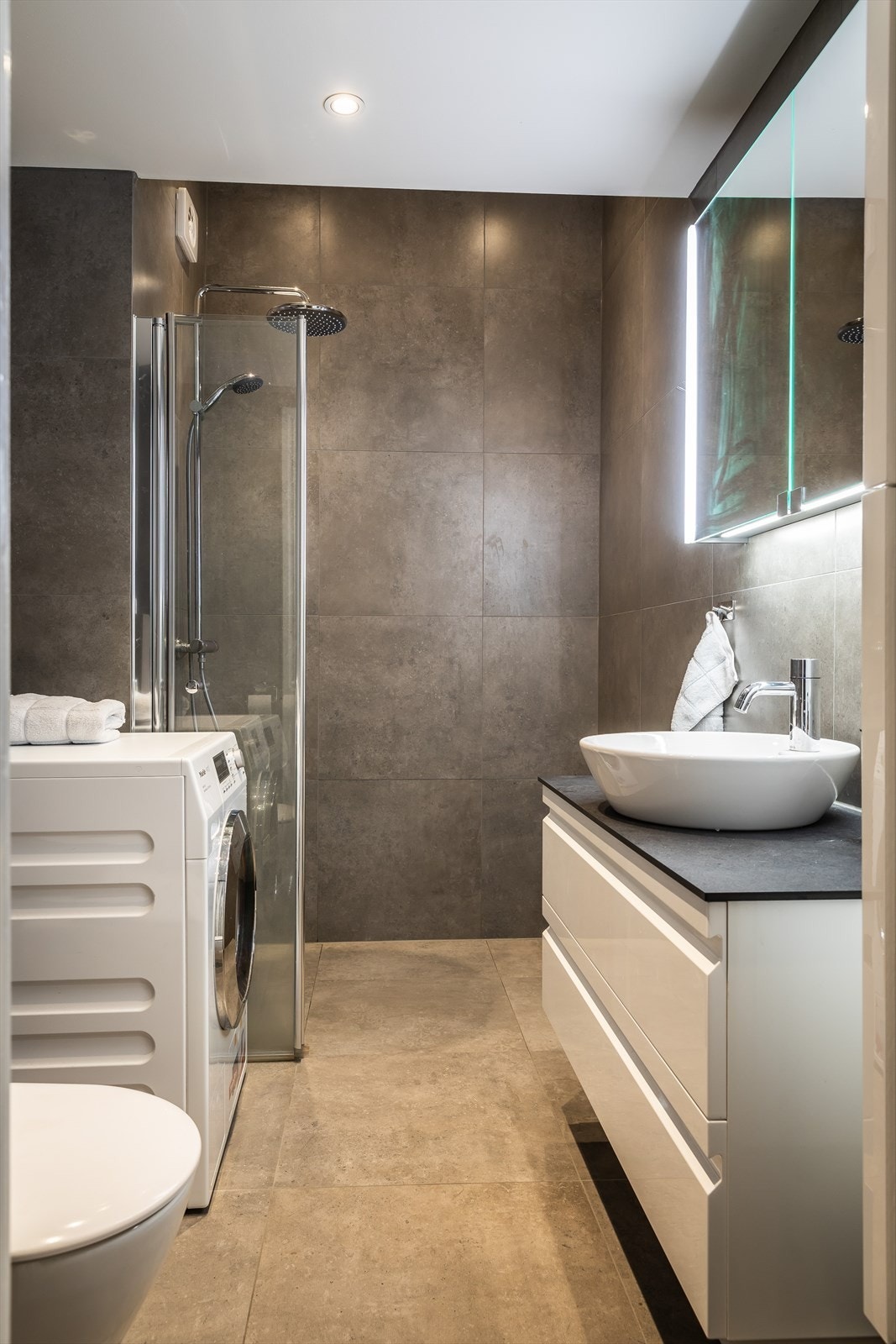 Baderomsinnredning bestående av benkeskap, veggskap, veggskap har speilfronter med integrert belysning, høyskap ved siden av servantskap. Galleribilde